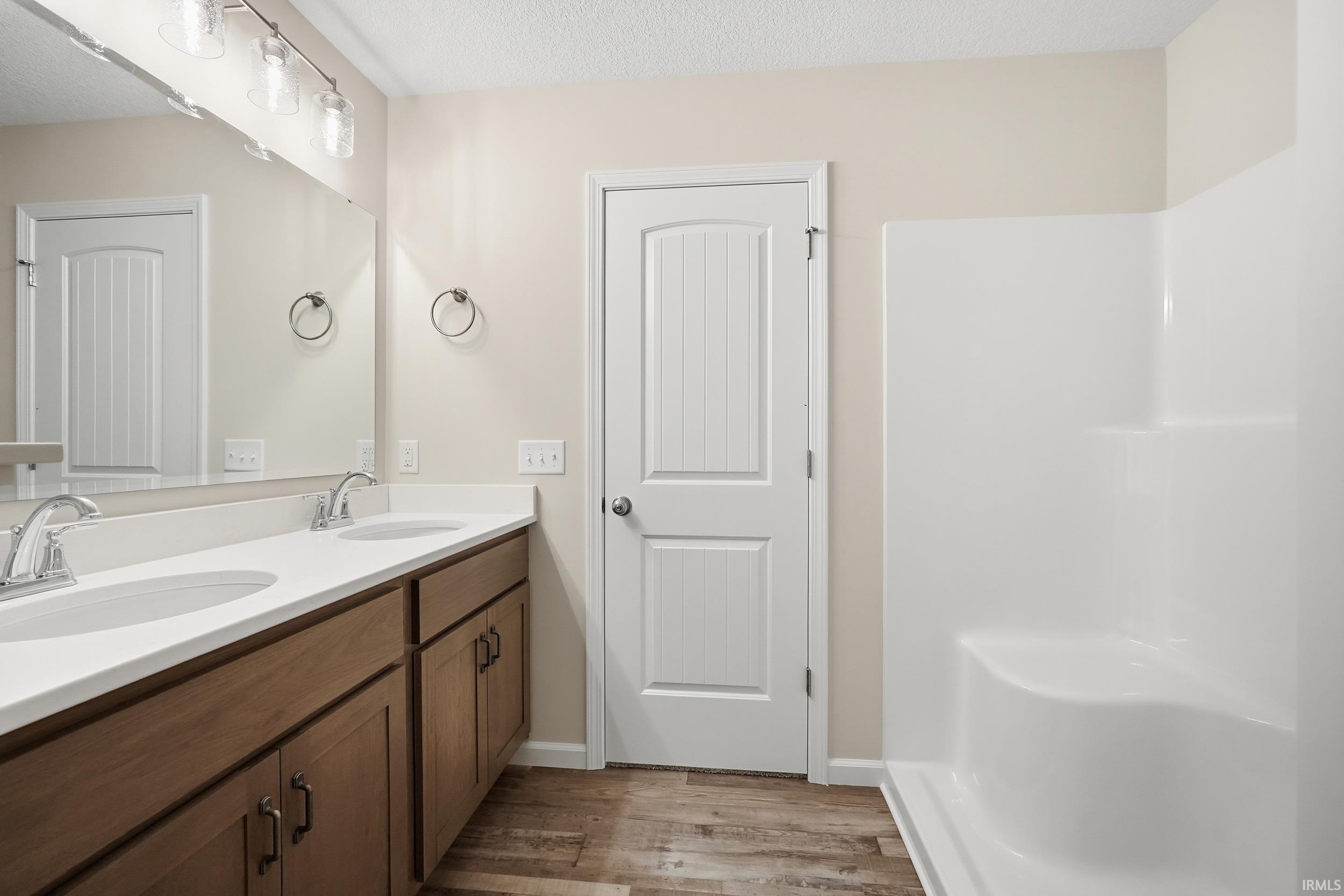 Full bathroom with double vanity, light wood-style flooring, a textured ceiling, and a shower