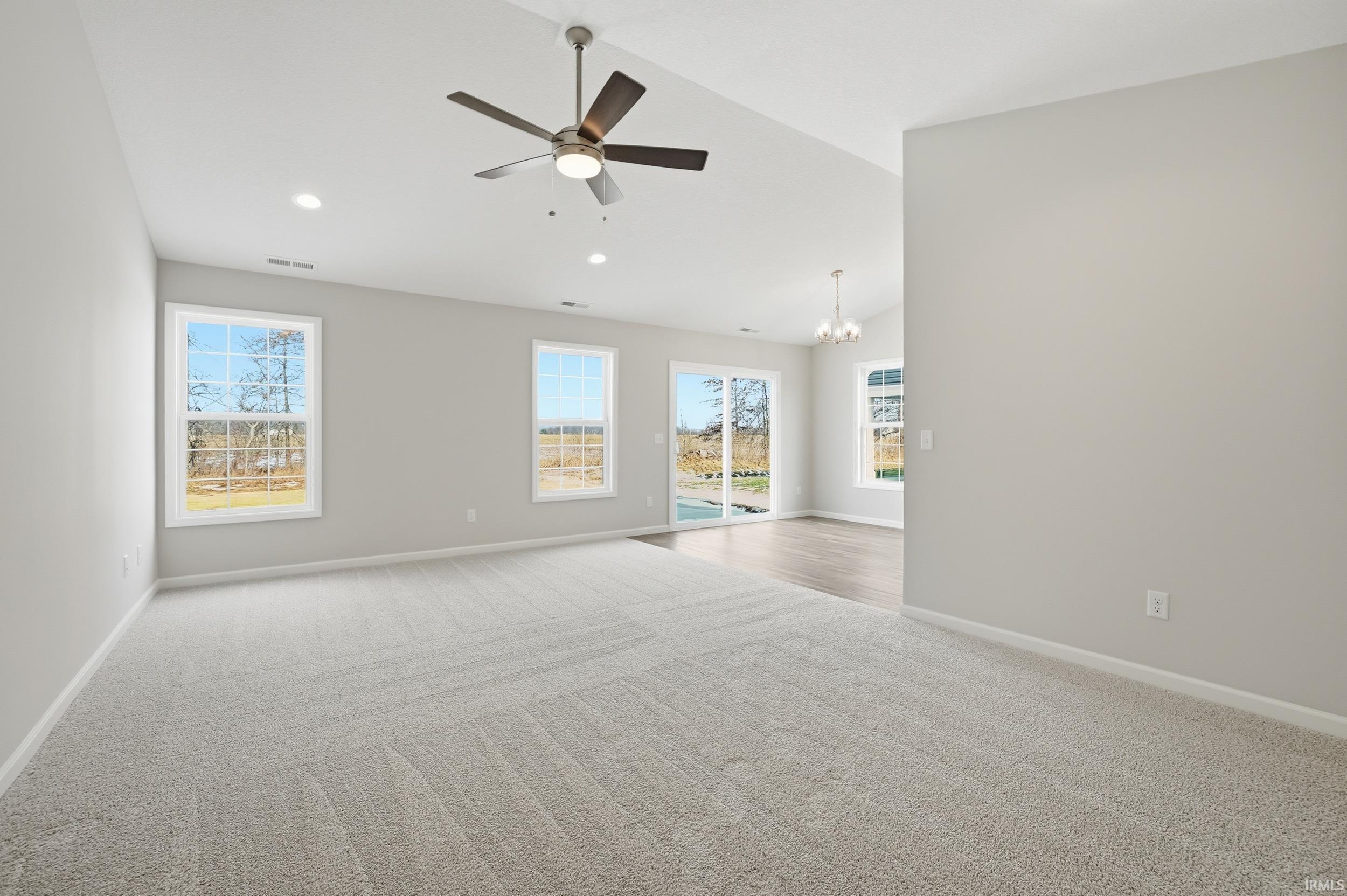 Carpeted empty room with a chandelier, lofted ceiling, a ceiling fan, healthy amount of natural light, and recessed lighting