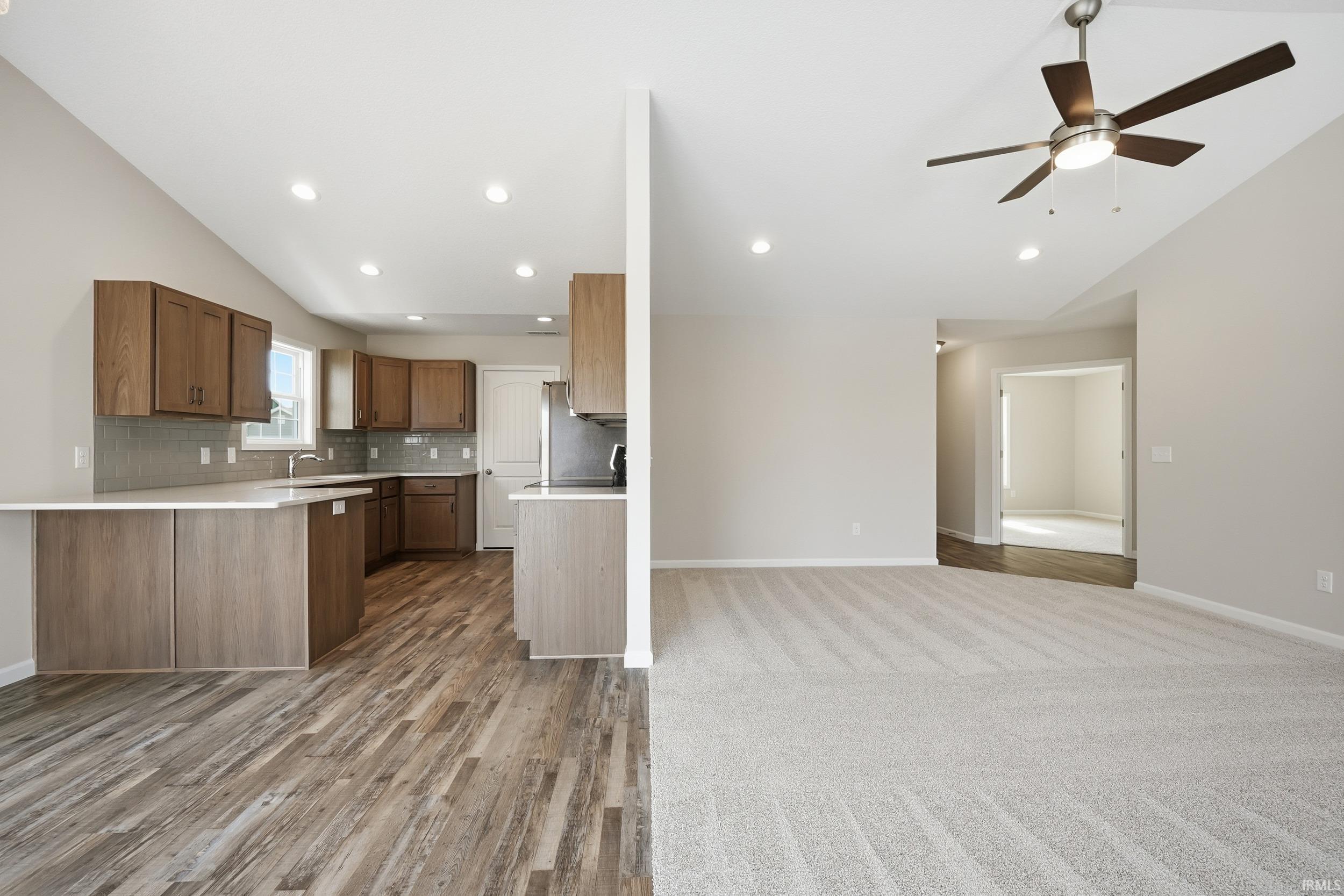 Kitchen with lofted ceiling, open floor plan, light countertops, backsplash, and ceiling fan