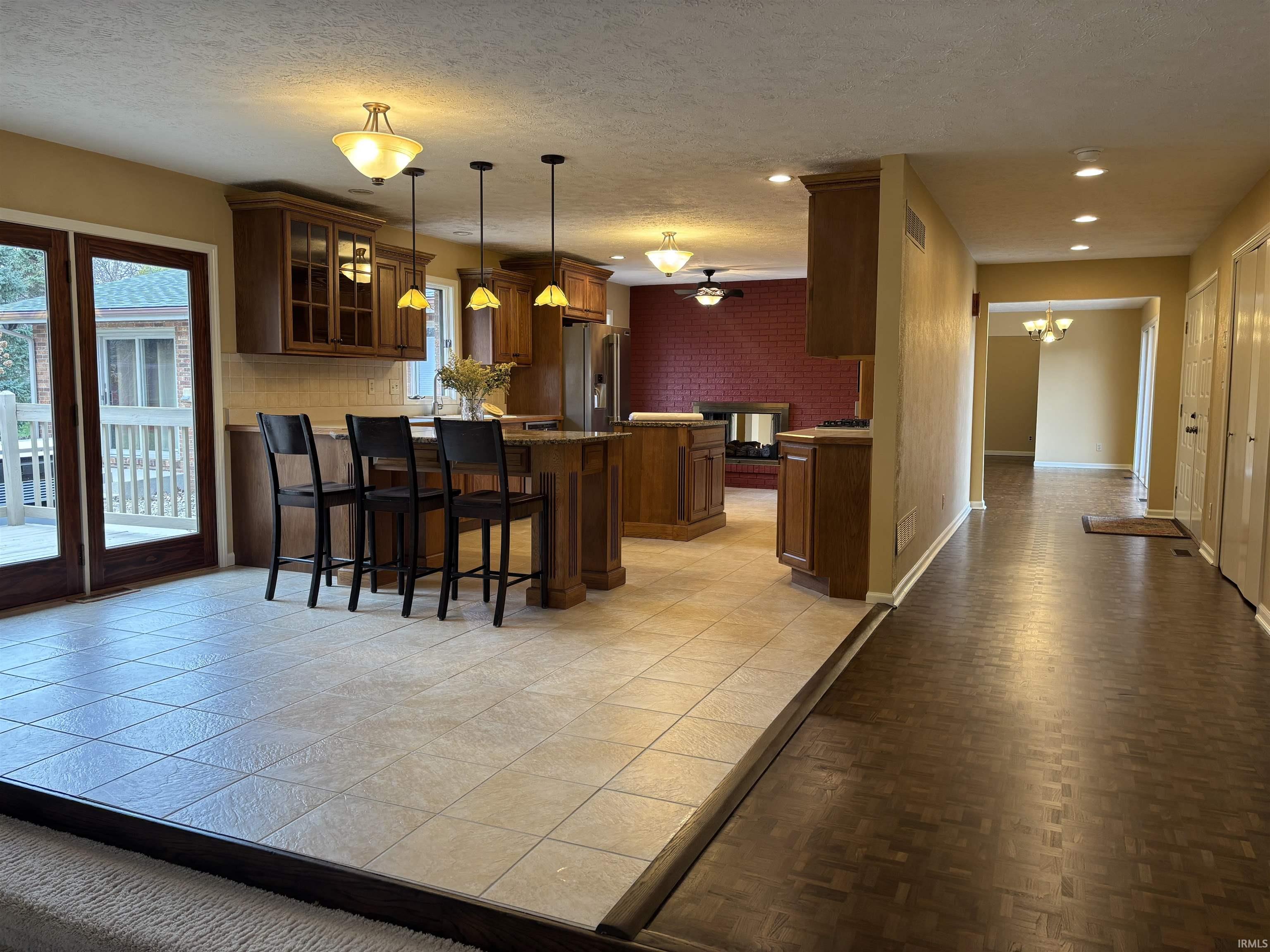 Kitchen with a textured ceiling, glass insert cabinets, a kitchen bar, a chandelier, and high end fridge