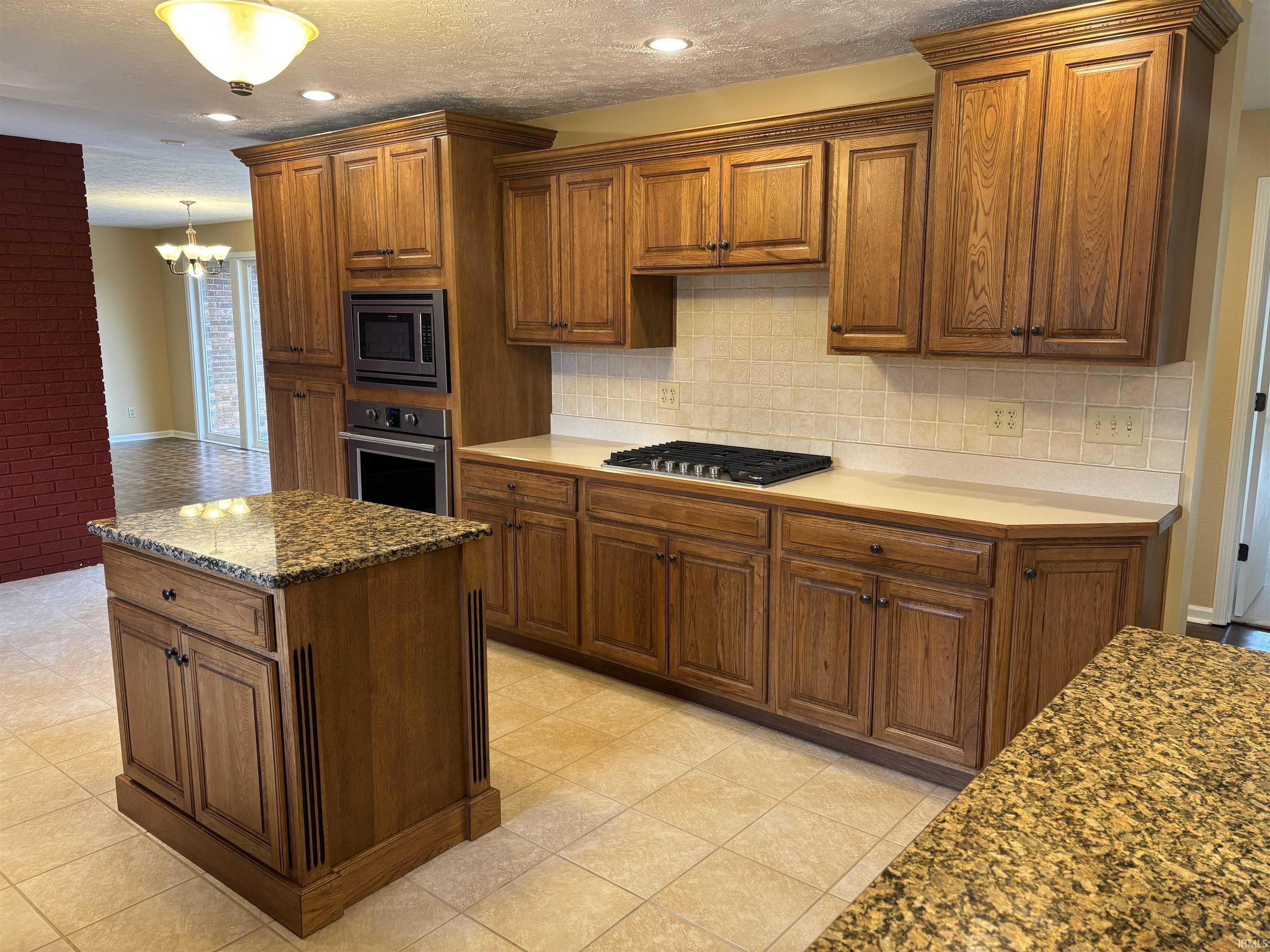 Kitchen with wood finish cabinetry, stainless steel appliances, a kitchen island, tasteful backsplash, and light tile patterned floors