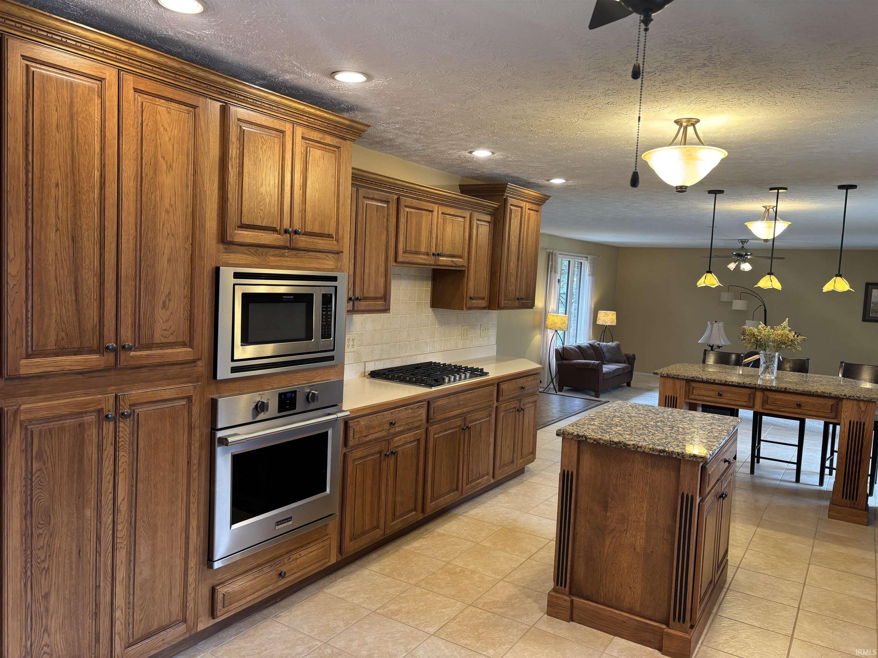 Kitchen with hanging light fixtures, a kitchen island, stainless steel appliances, wood finish cabinetry, and backsplash