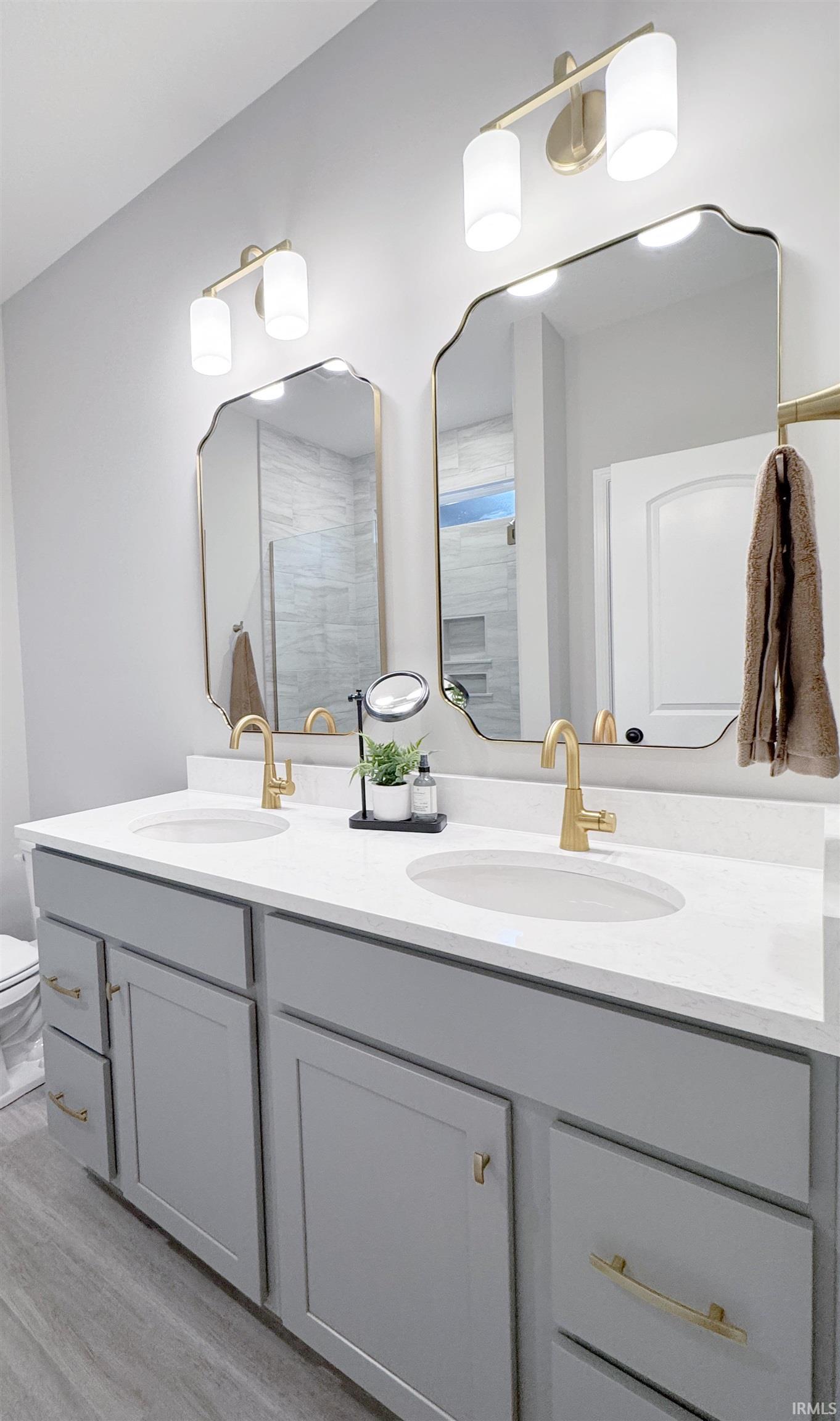 Owner Suite Bathroom with double vanity, a tile shower, and light wood-style floors