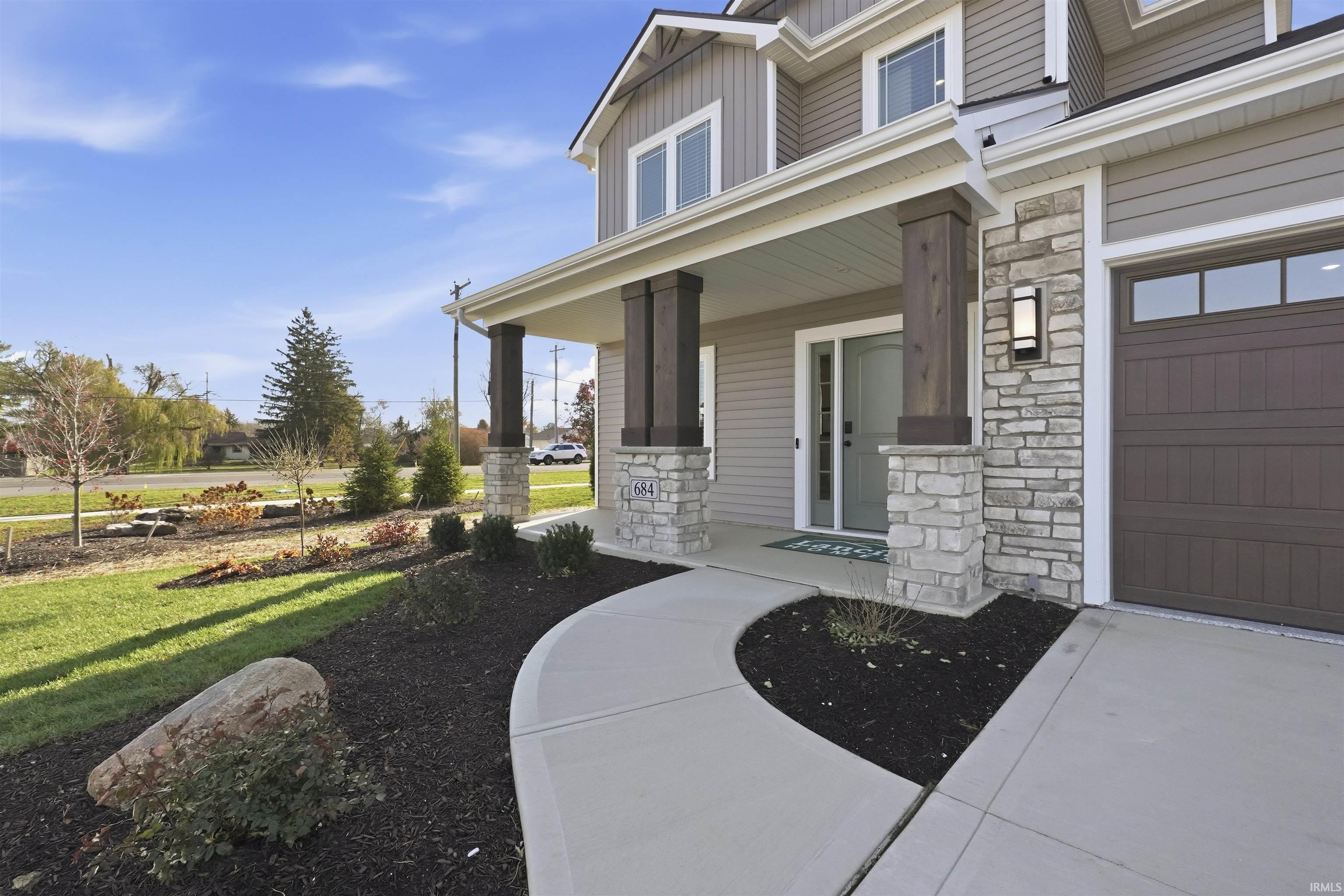Entrance to property featuring covered porch, stone siding, a garage, and board and batten siding