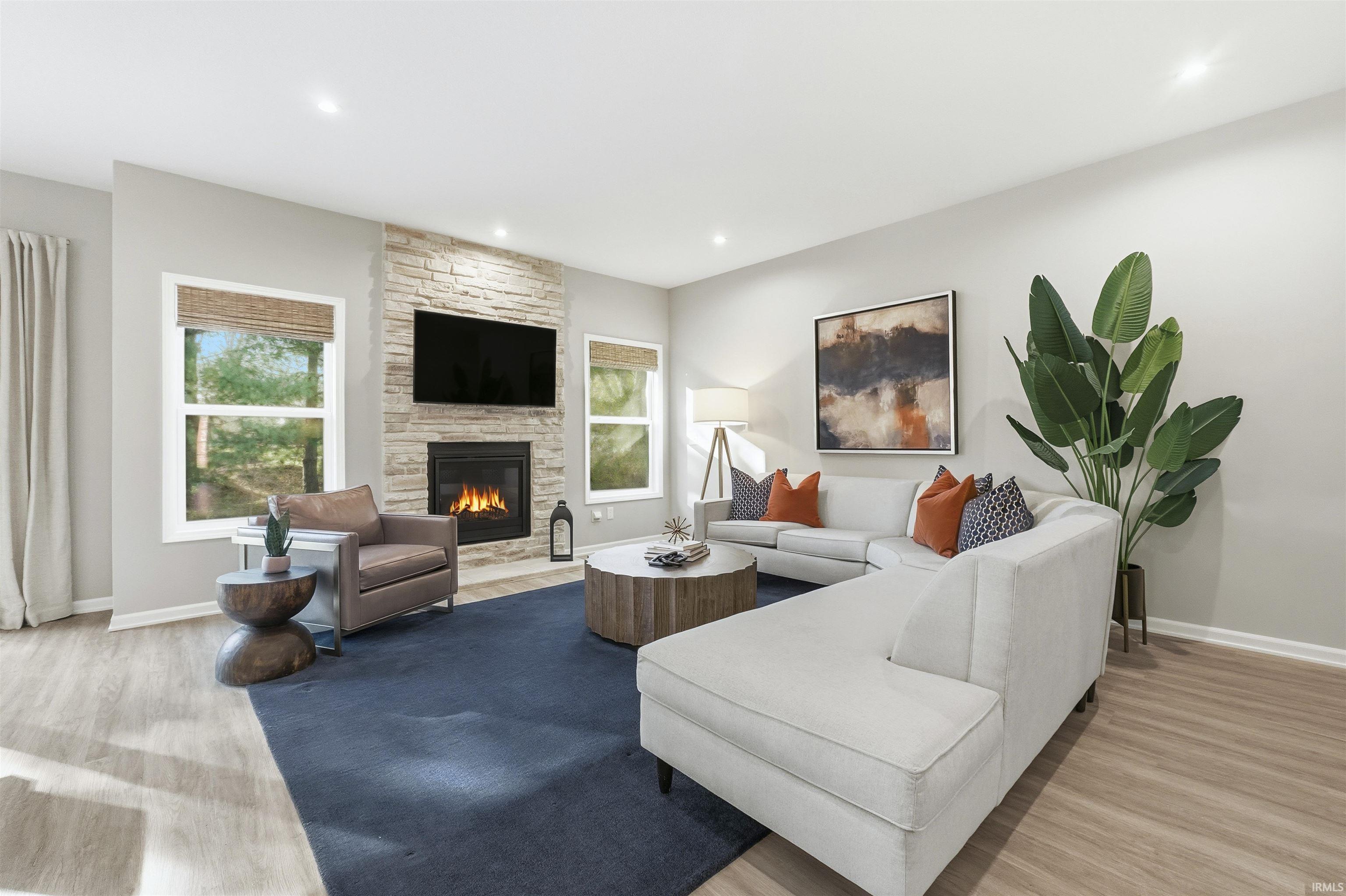 Great Room featuring plenty of natural light, light wood-style flooring, a stone fireplace, and recessed lighting