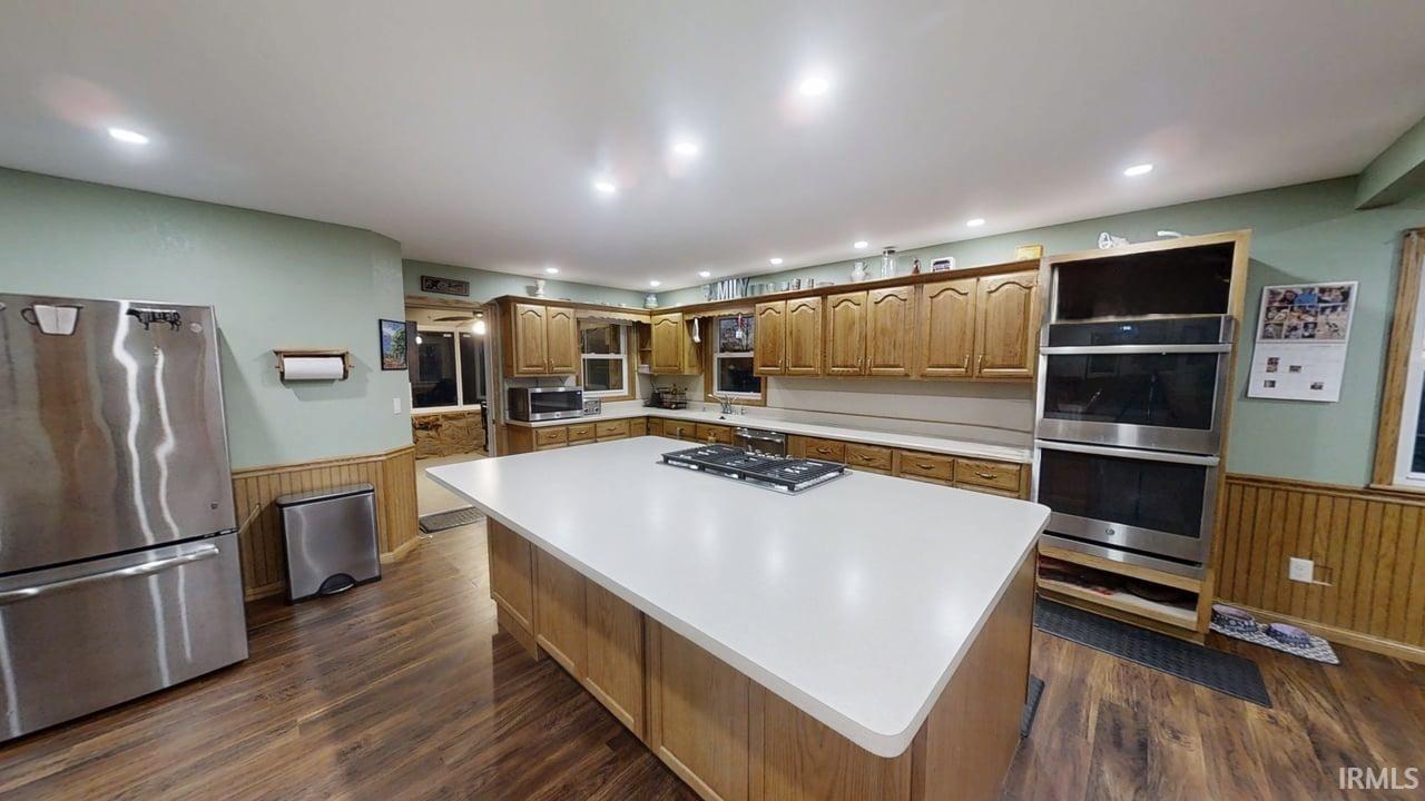 Kitchen featuring wainscoting, stainless steel appliances, massive center island, and light countertops