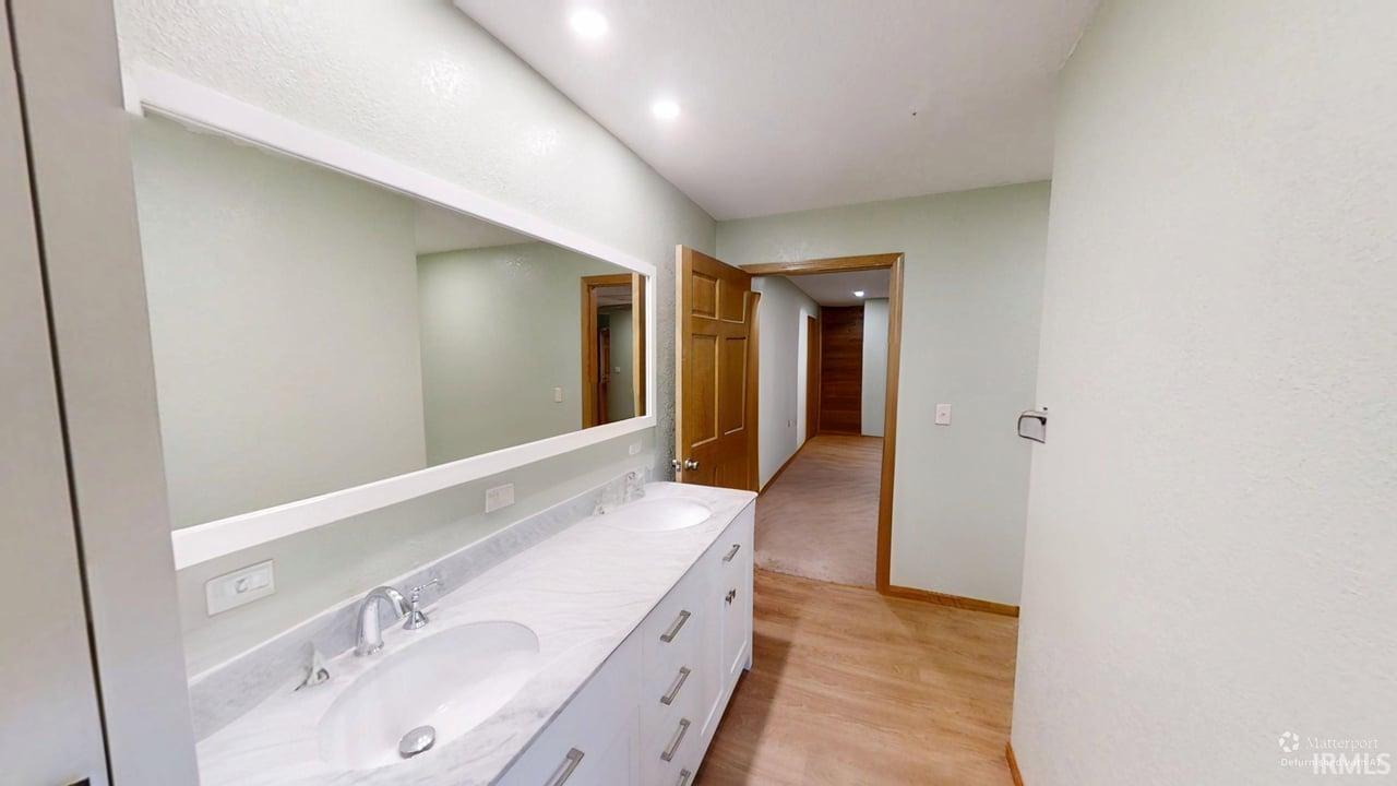 Bathroom featuring double vanity, light wood finished floors, and recessed lighting