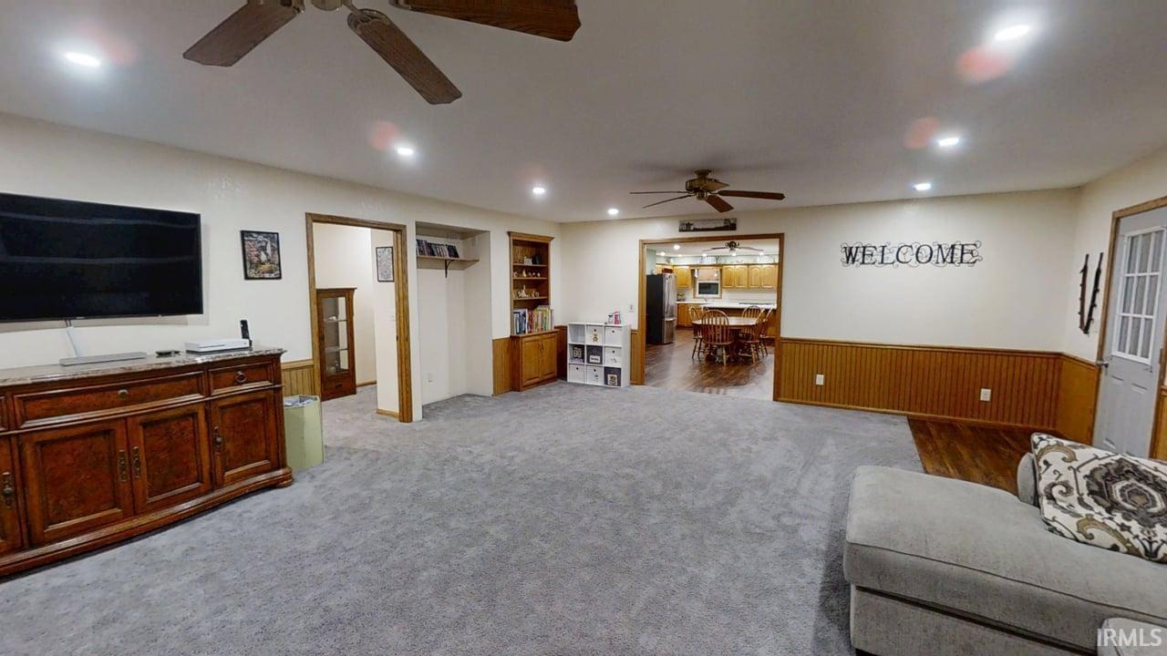 Living room featuring a ceiling fan, wainscoting, light colored carpet, and recessed lighting