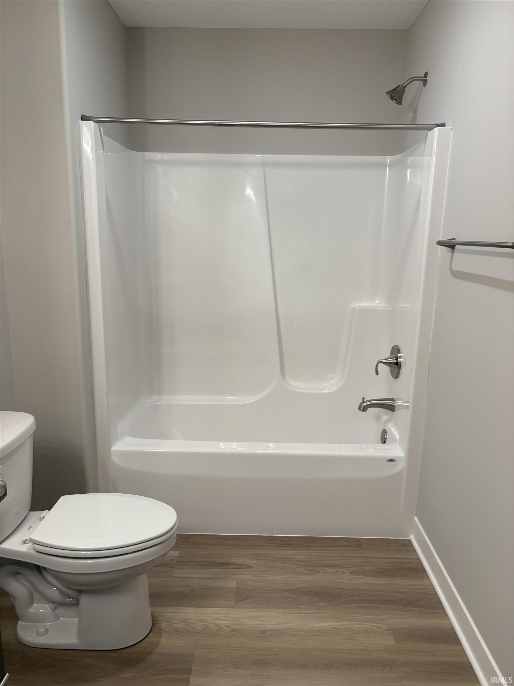 Bathroom featuring a white bathtub/shower combination with chrome fixtures, wood-finish flooring, a white toilet, and light-toned walls