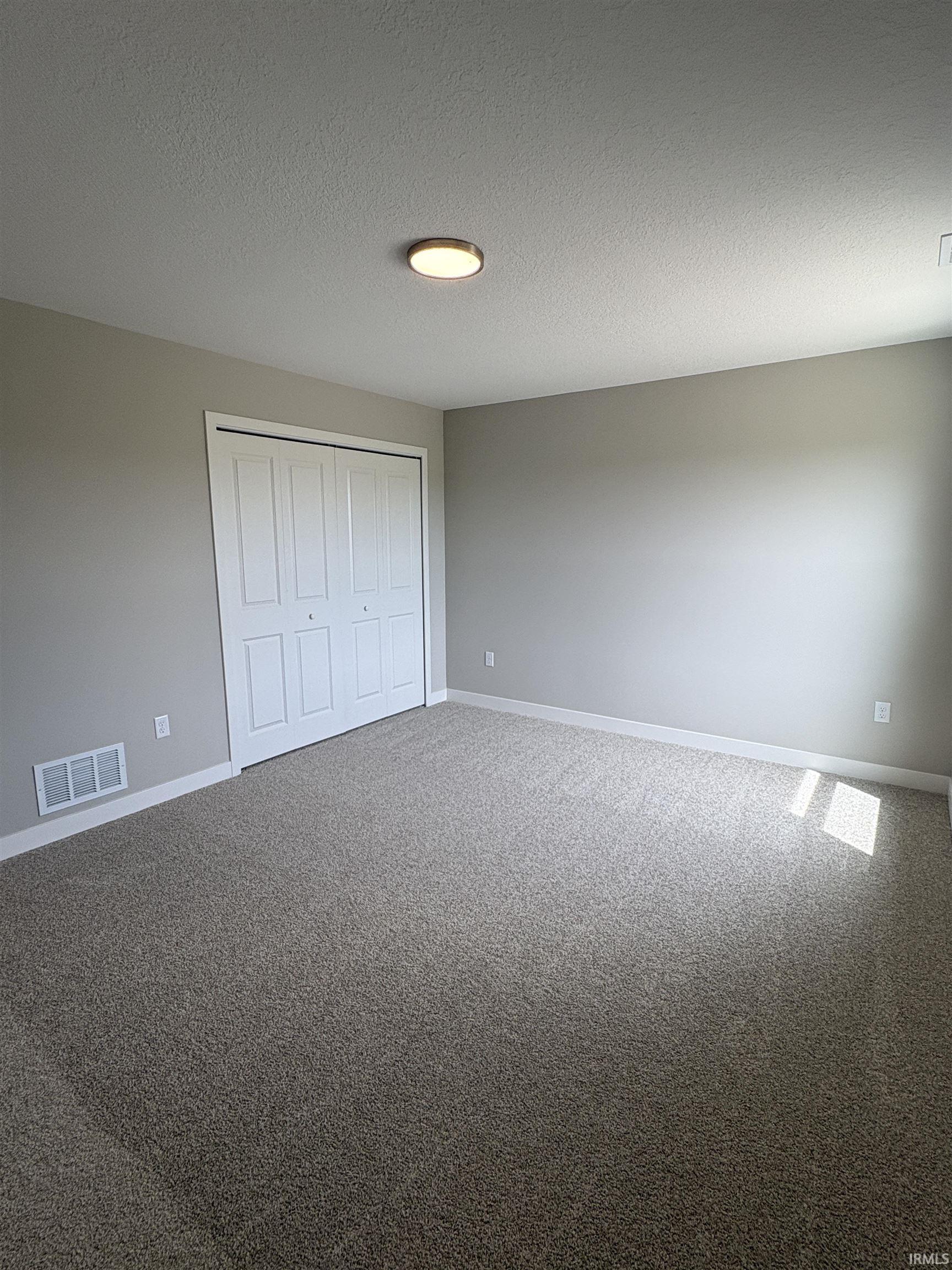 Carpeted room featuring neutral wall tones, white baseboards, and a bi-fold closet