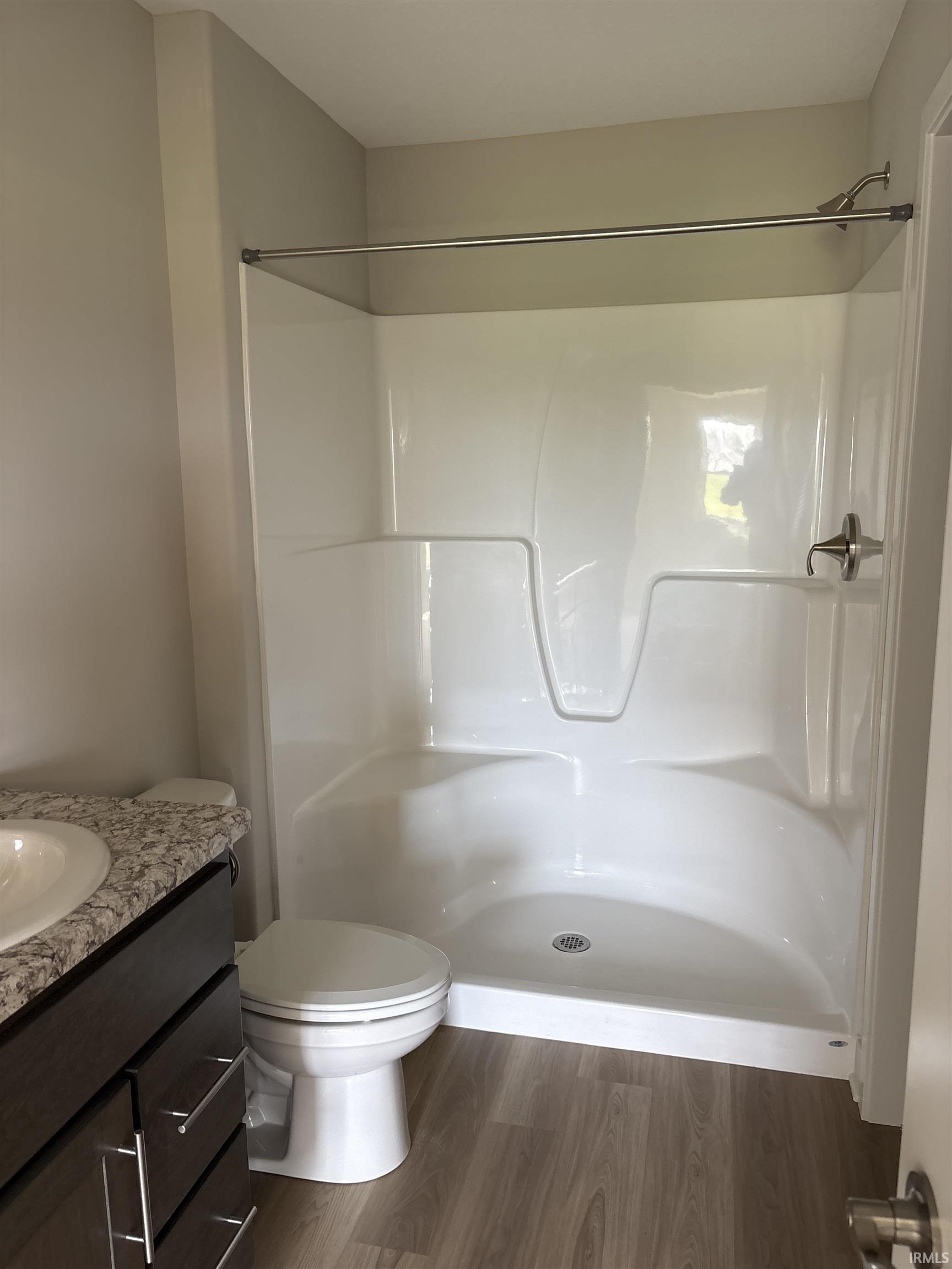 Bathroom featuring a white shower stall, a toilet, a vanity with a granite-style countertop, and wood-finish flooring