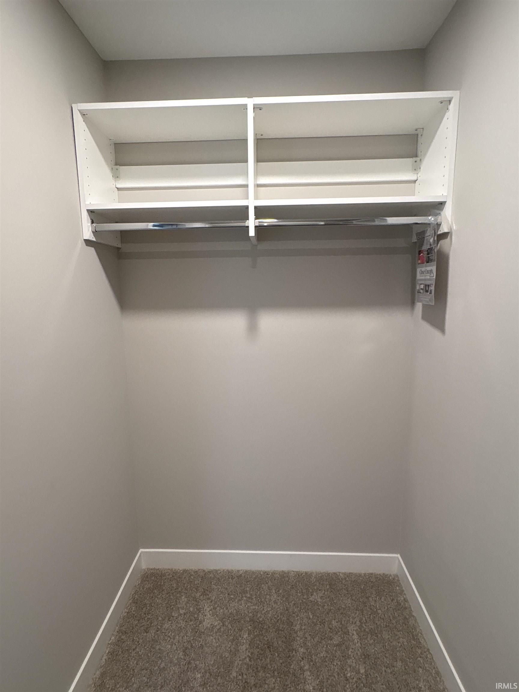 Closet interior featuring built-in white shelving, a chrome hanging rod, neutral wall paint, white baseboards, and brown carpeting