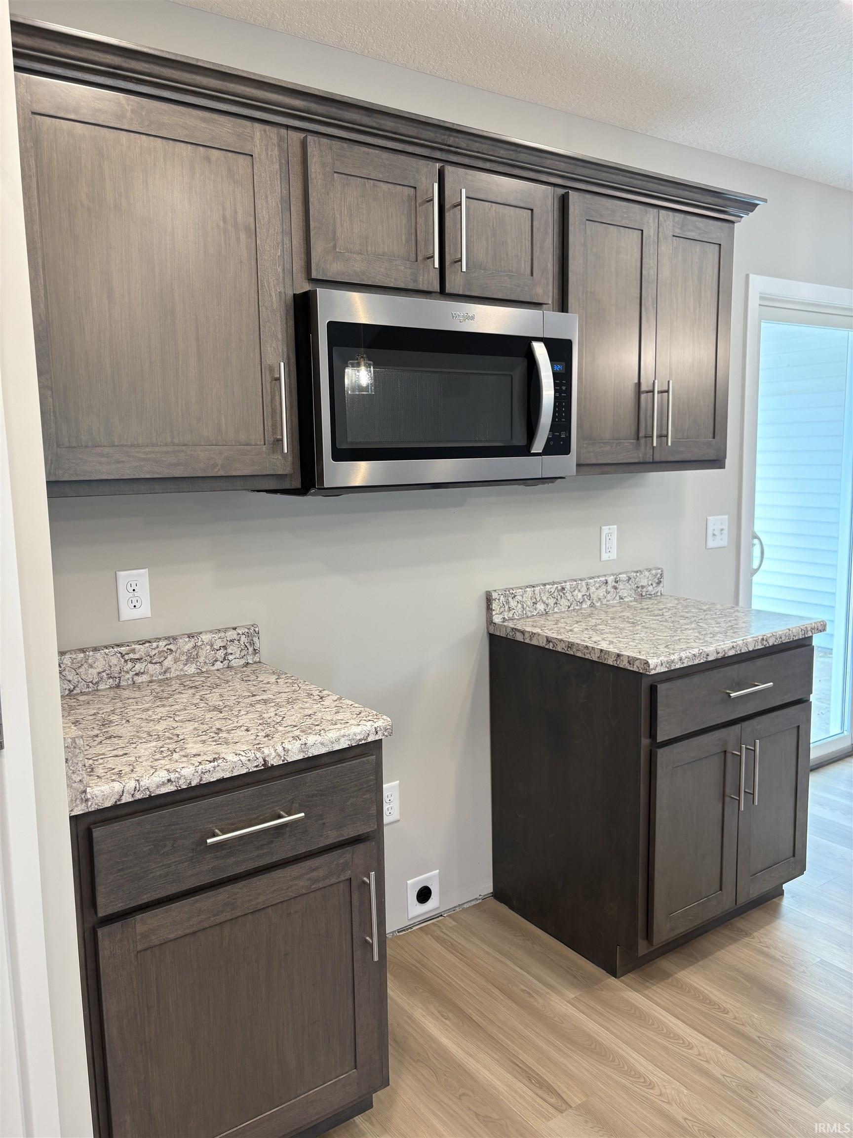 Kitchen area featuring wood-finish flooring, gray shaker-style cabinetry with crown molding, stainless steel microwave, and light-toned countertops