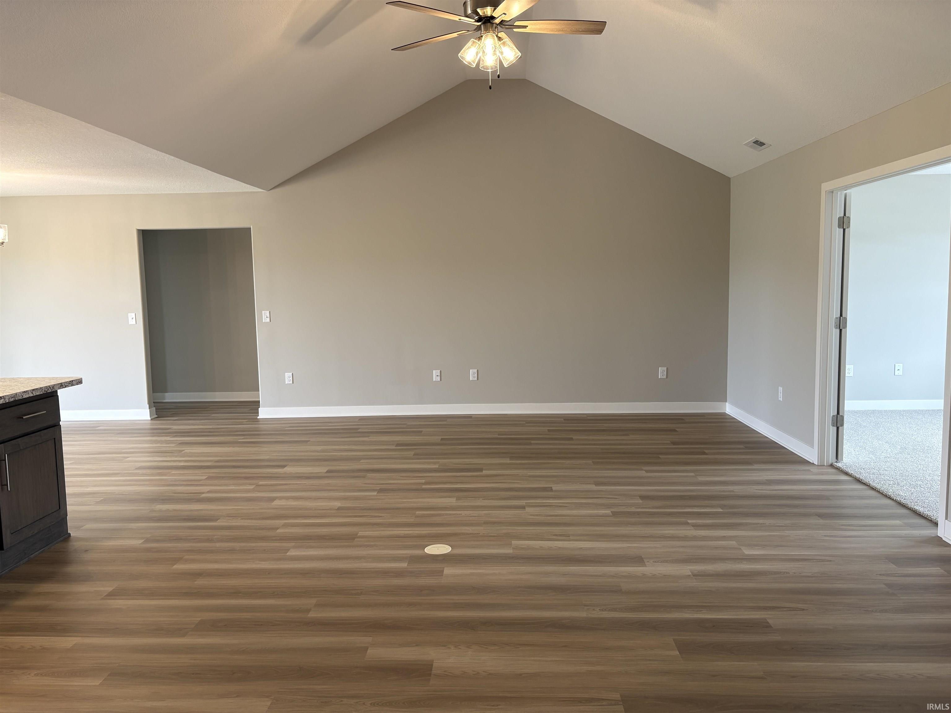 Open concept living area featuring wood-finish flooring, vaulted ceilings, and a ceiling fan with integrated lighting