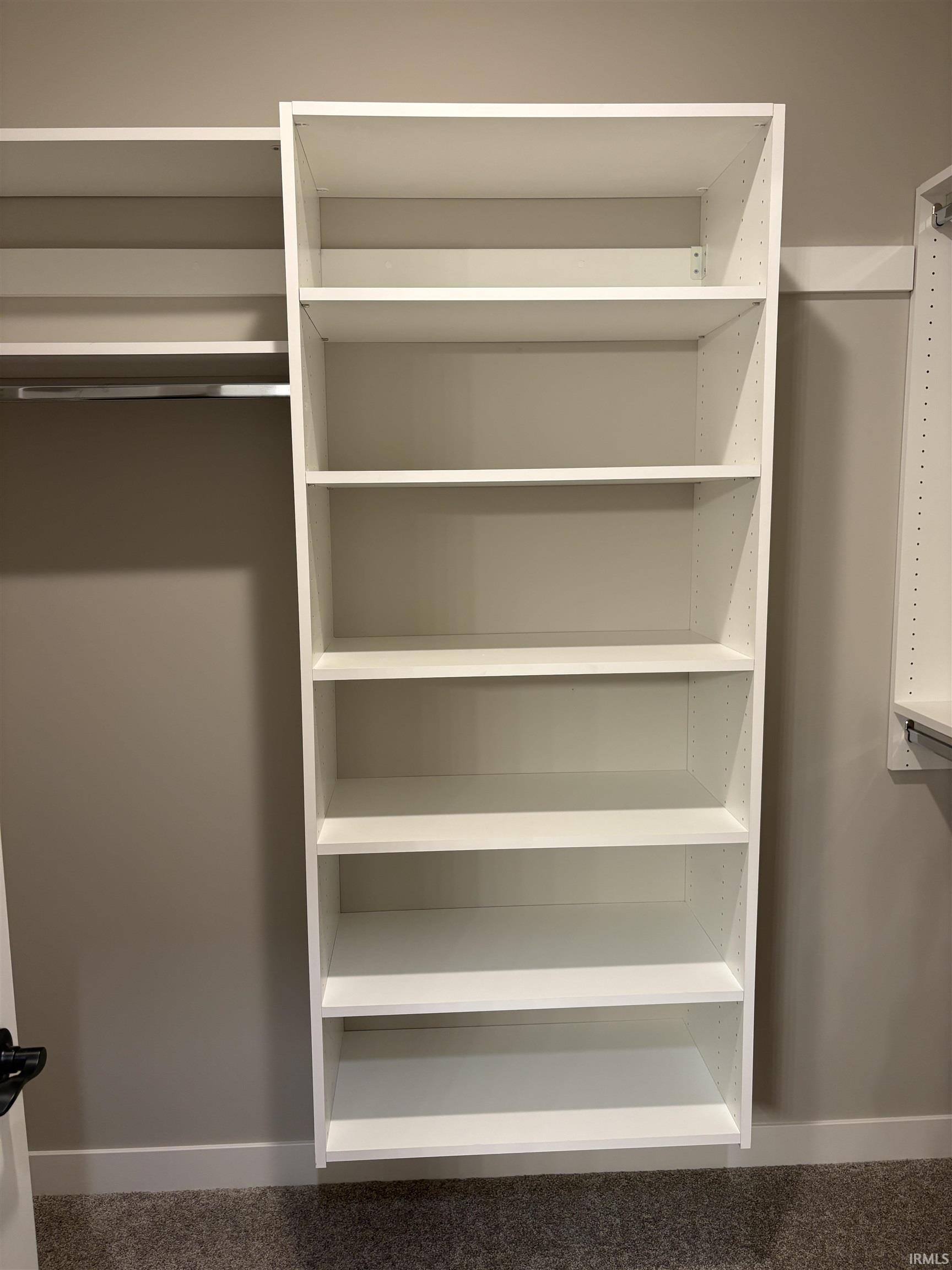 Built-in closet shelving system featuring multiple white shelves, a clothing rod, and neutral-toned carpeting
