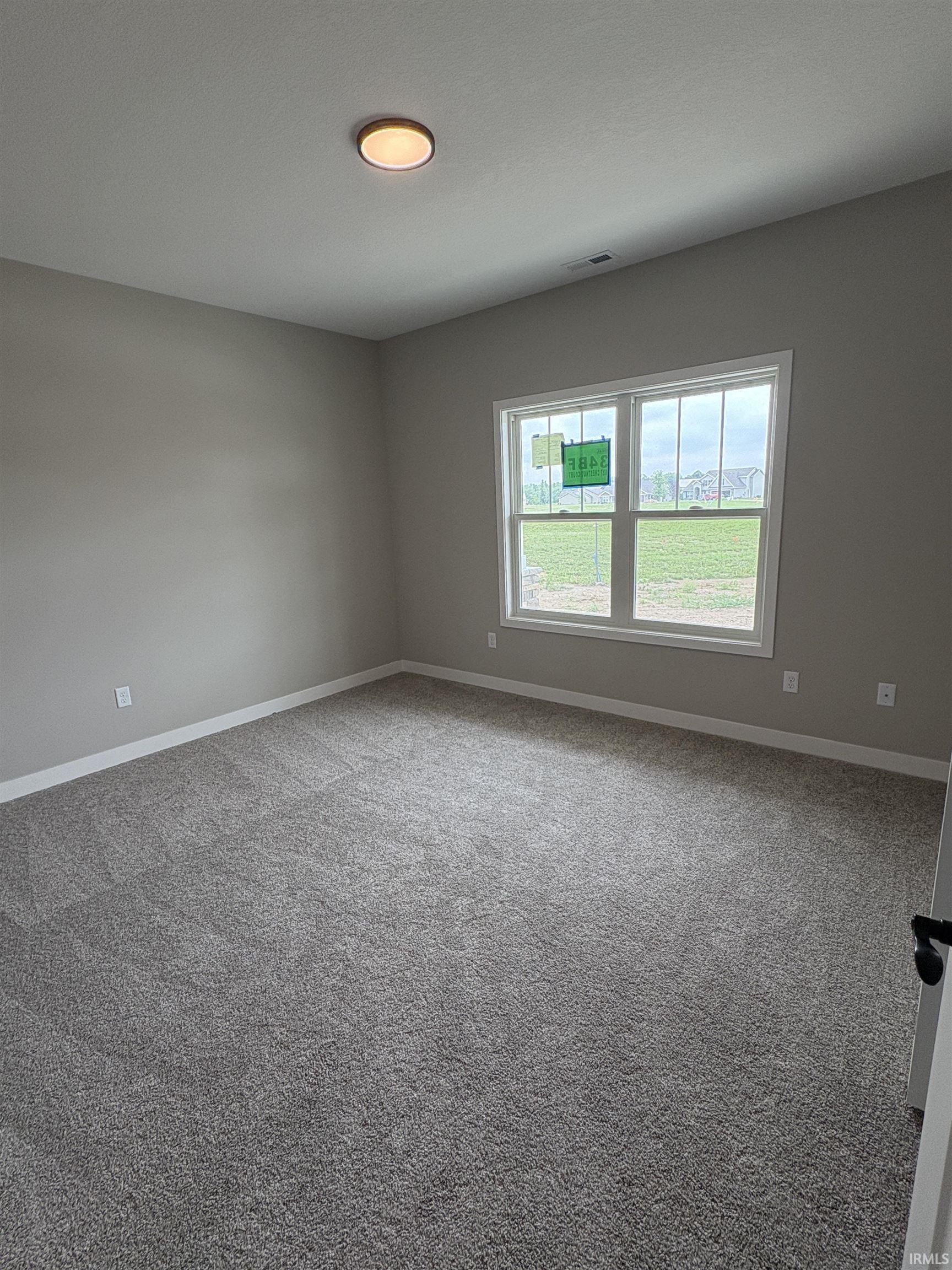 Spacious room featuring neutral tone walls, new gray carpet, white trim, and a double-paned window