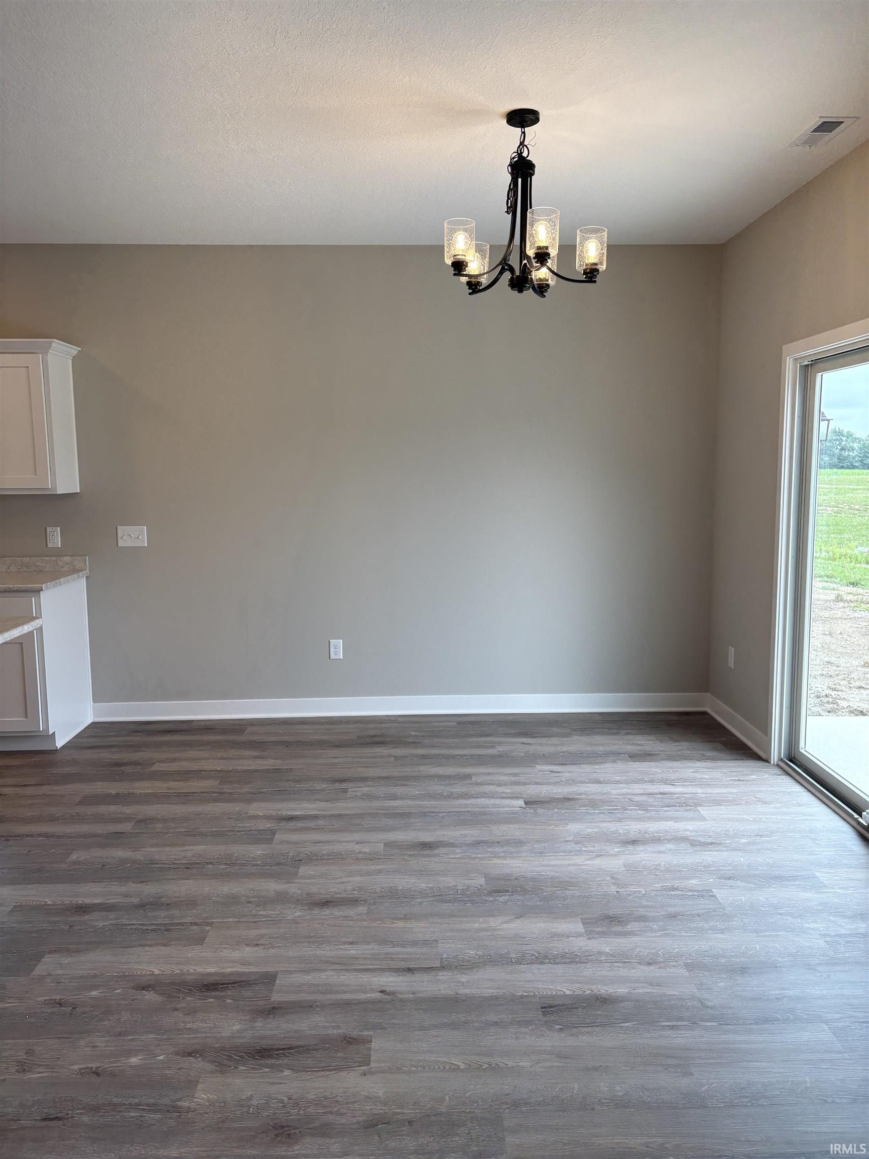 Dining area featuring wood-finish flooring, a contemporary black chandelier, neutral wall tones, white baseboards, and a sliding glass door