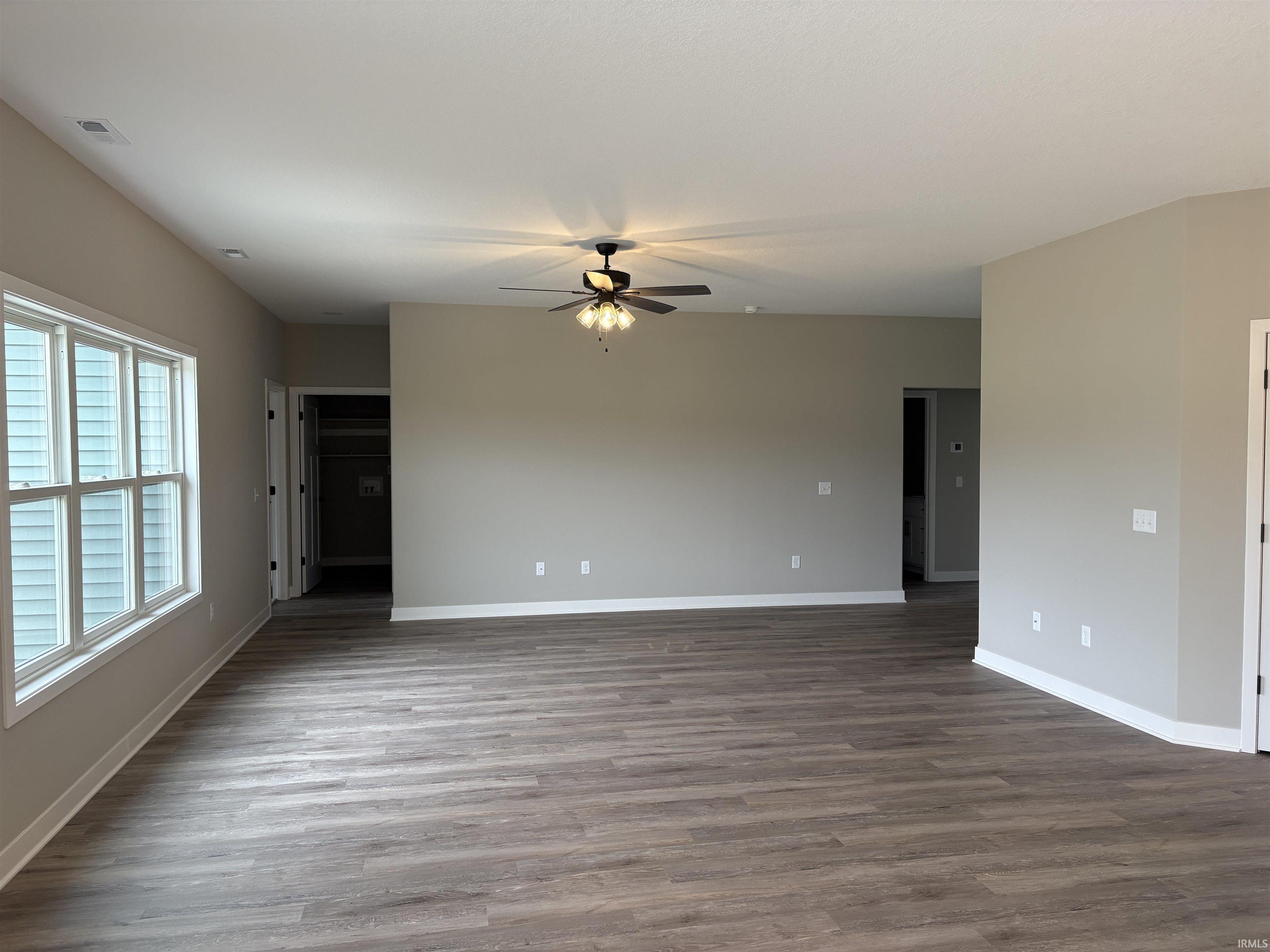 Spacious room featuring wood-finish flooring, neutral paint palette, ample natural light from multiple windows, and a ceiling fan with integrated lighting