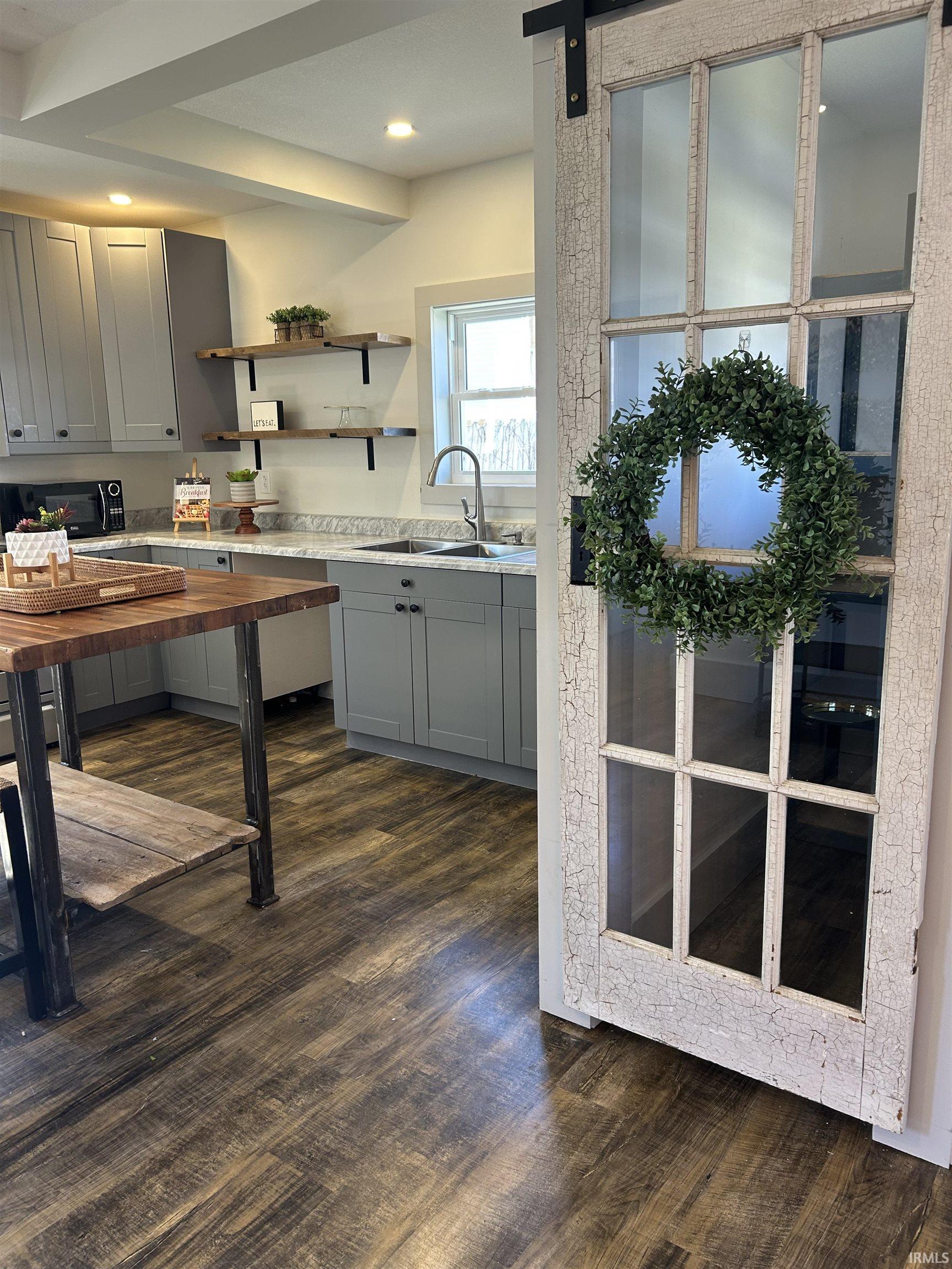 Kitchen with gray cabinetry, open shelves, a barn door, dark wood-style floors, and light stone countertops