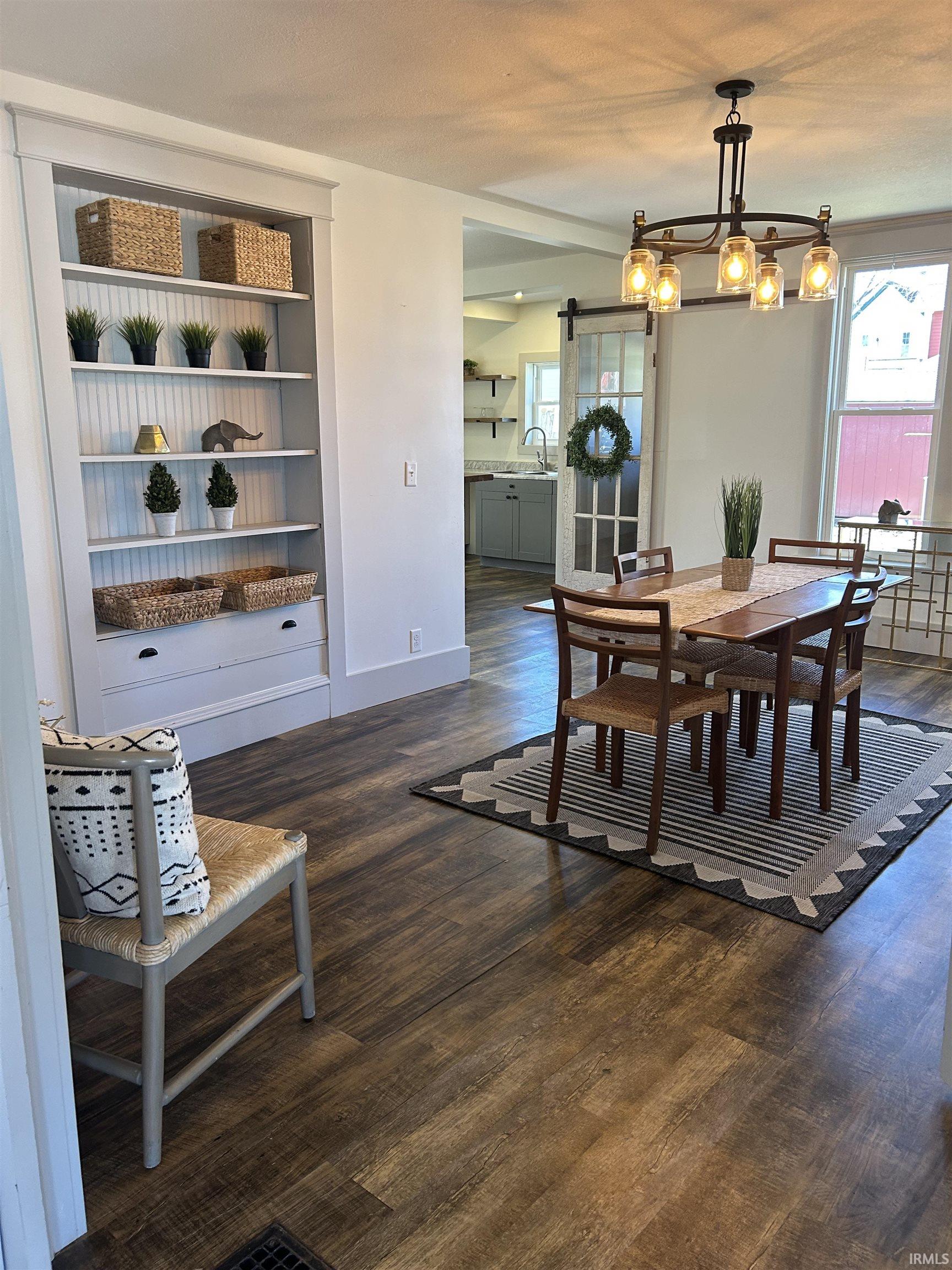 Dining area with a barn door, dark wood-style flooring, a chandelier, and built in shelves