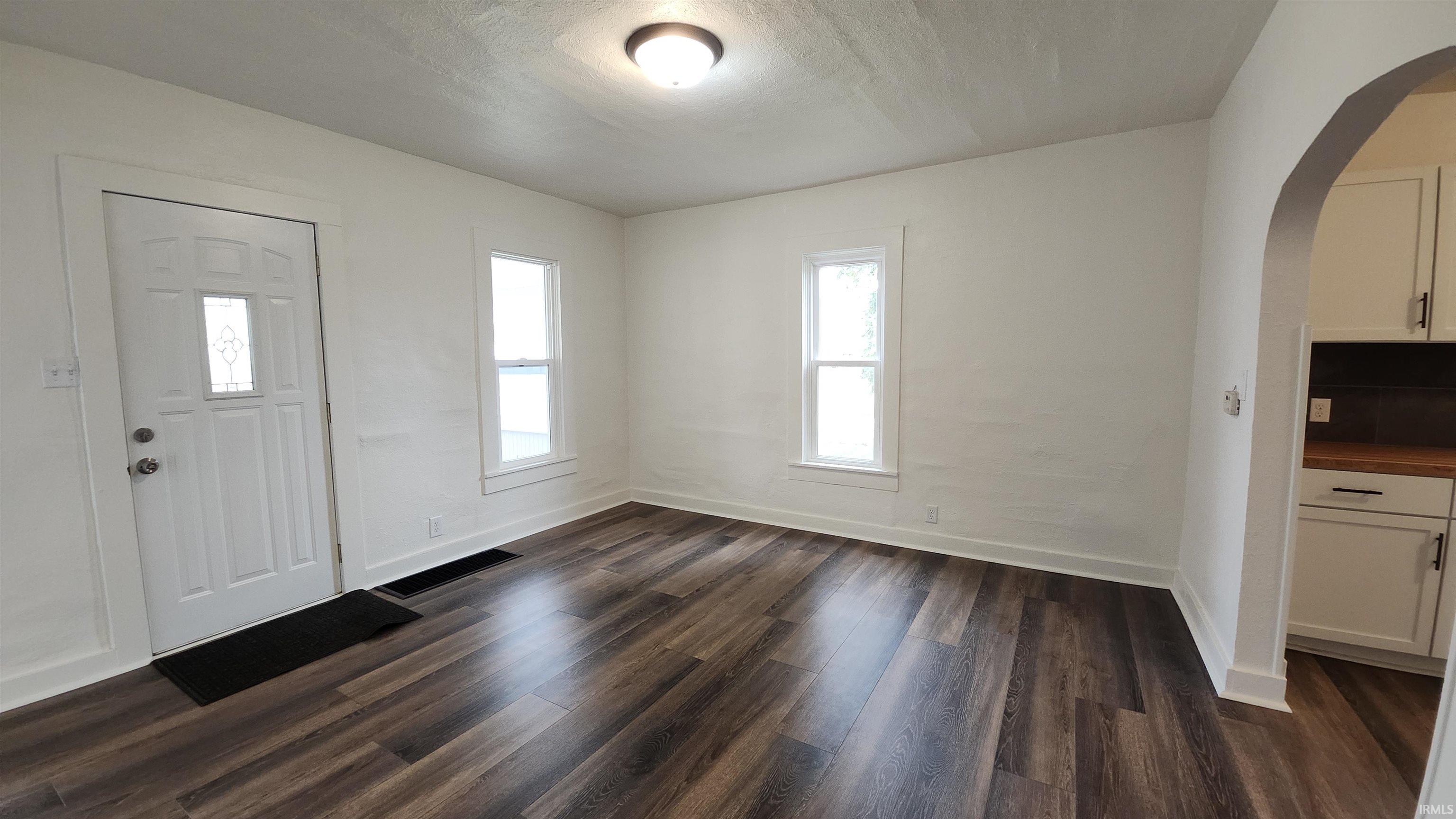 Entryway featuring arched walkways, dark wood-style flooring, and a textured ceiling