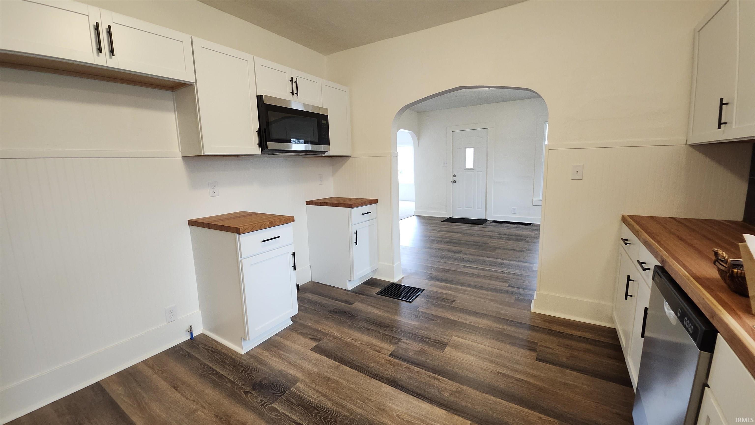 Kitchen with wood counters, white cabinetry, arched walkways, stainless steel appliances, and dark wood finished floors