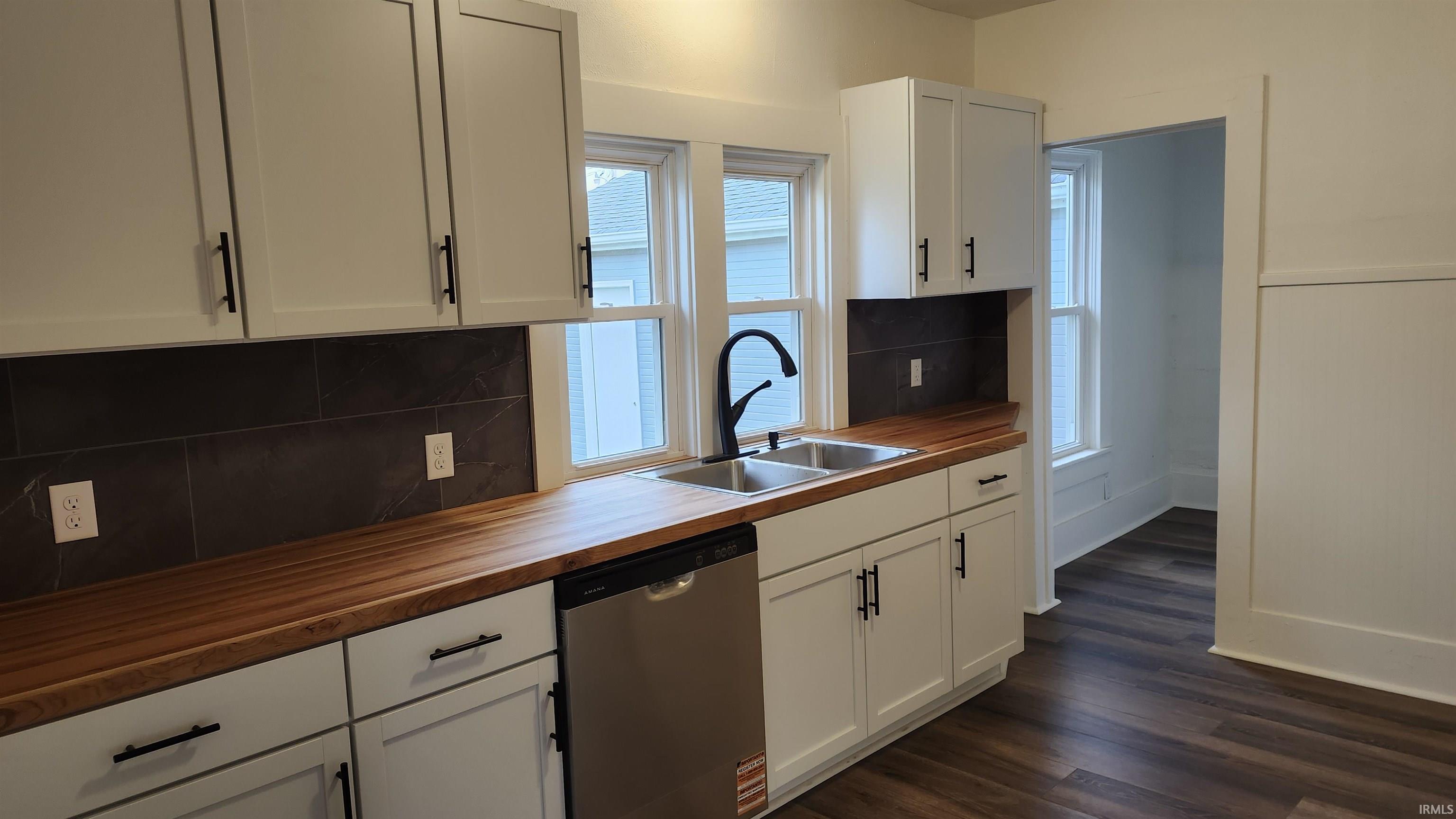 Kitchen featuring dishwasher, backsplash, white cabinets, dark wood-style floors, and wood counters