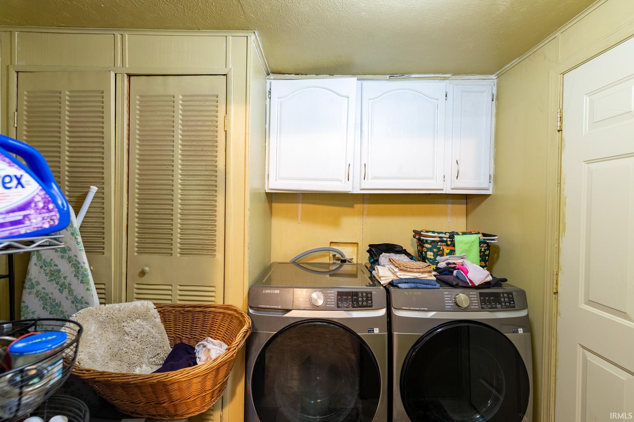 Laundry room with washer and clothes dryer, cabinet space, and a textured ceiling