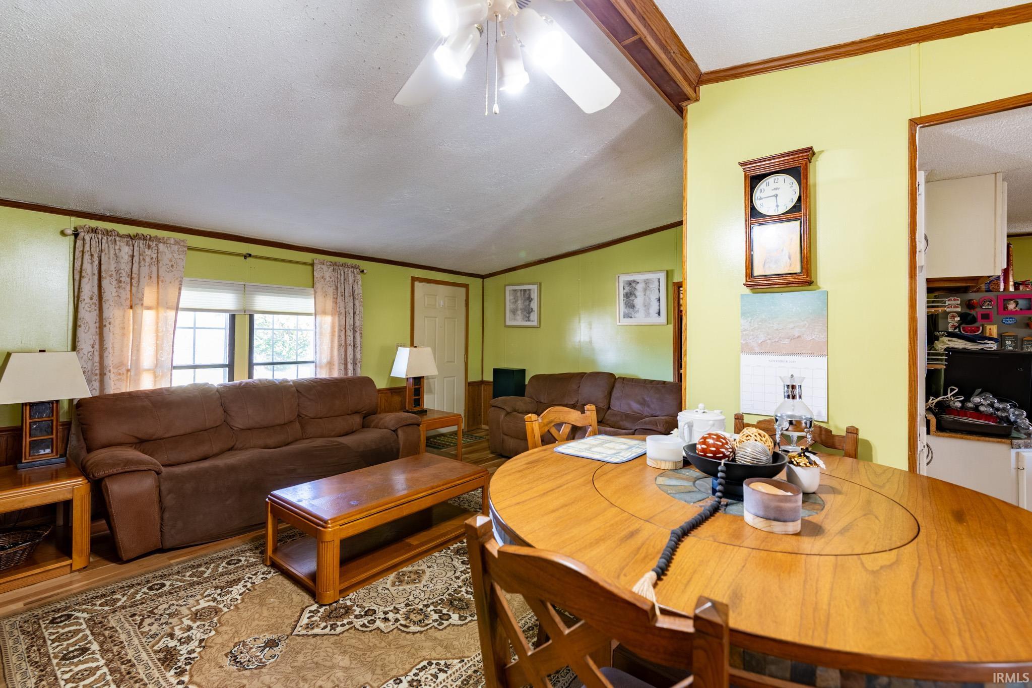 Dining room featuring crown molding, vaulted ceiling, a ceiling fan, wood finished floors, and a textured ceiling