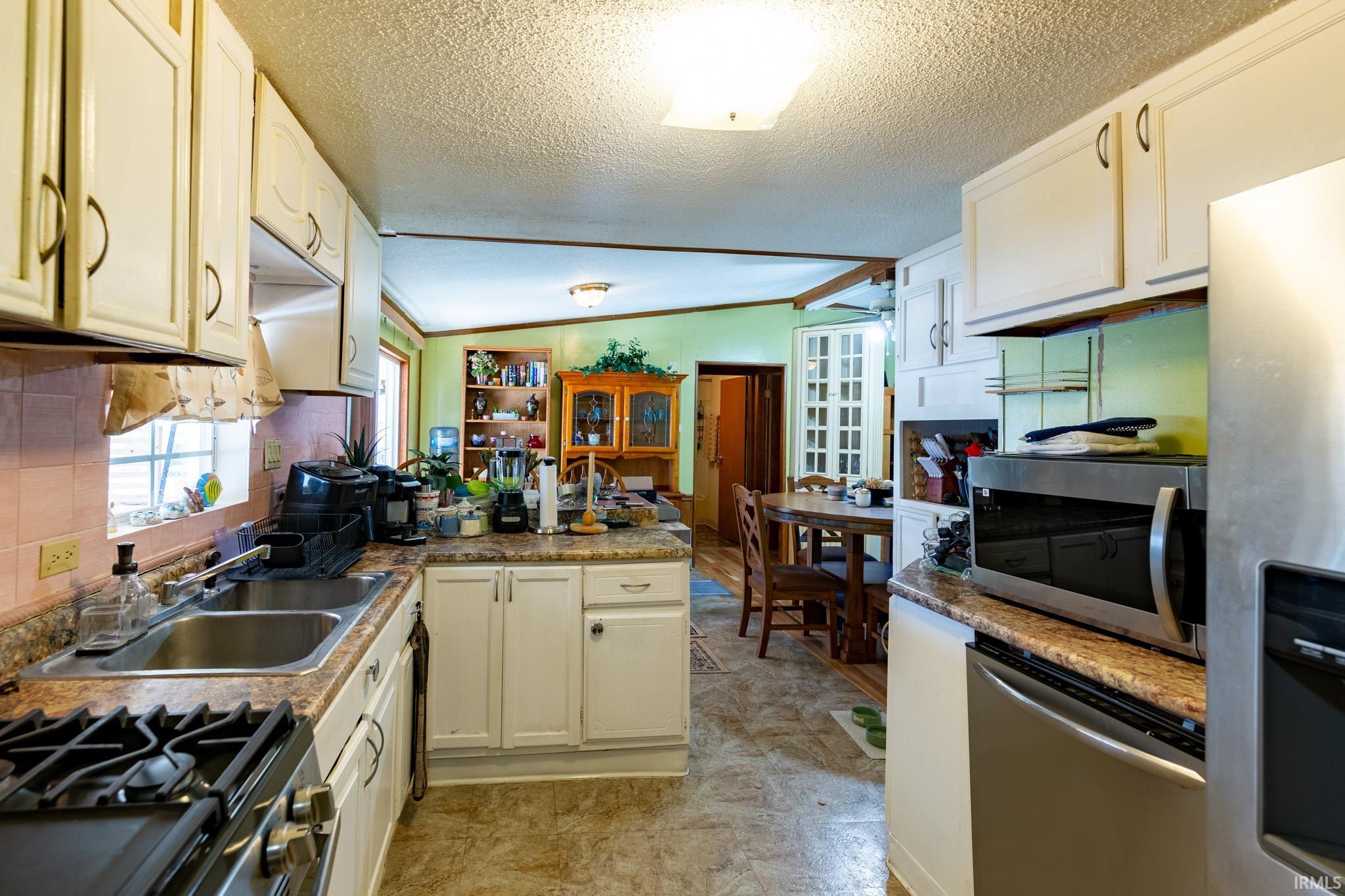 Kitchen with a peninsula, appliances with stainless steel finishes, lofted ceiling, a textured ceiling, and tasteful backsplash