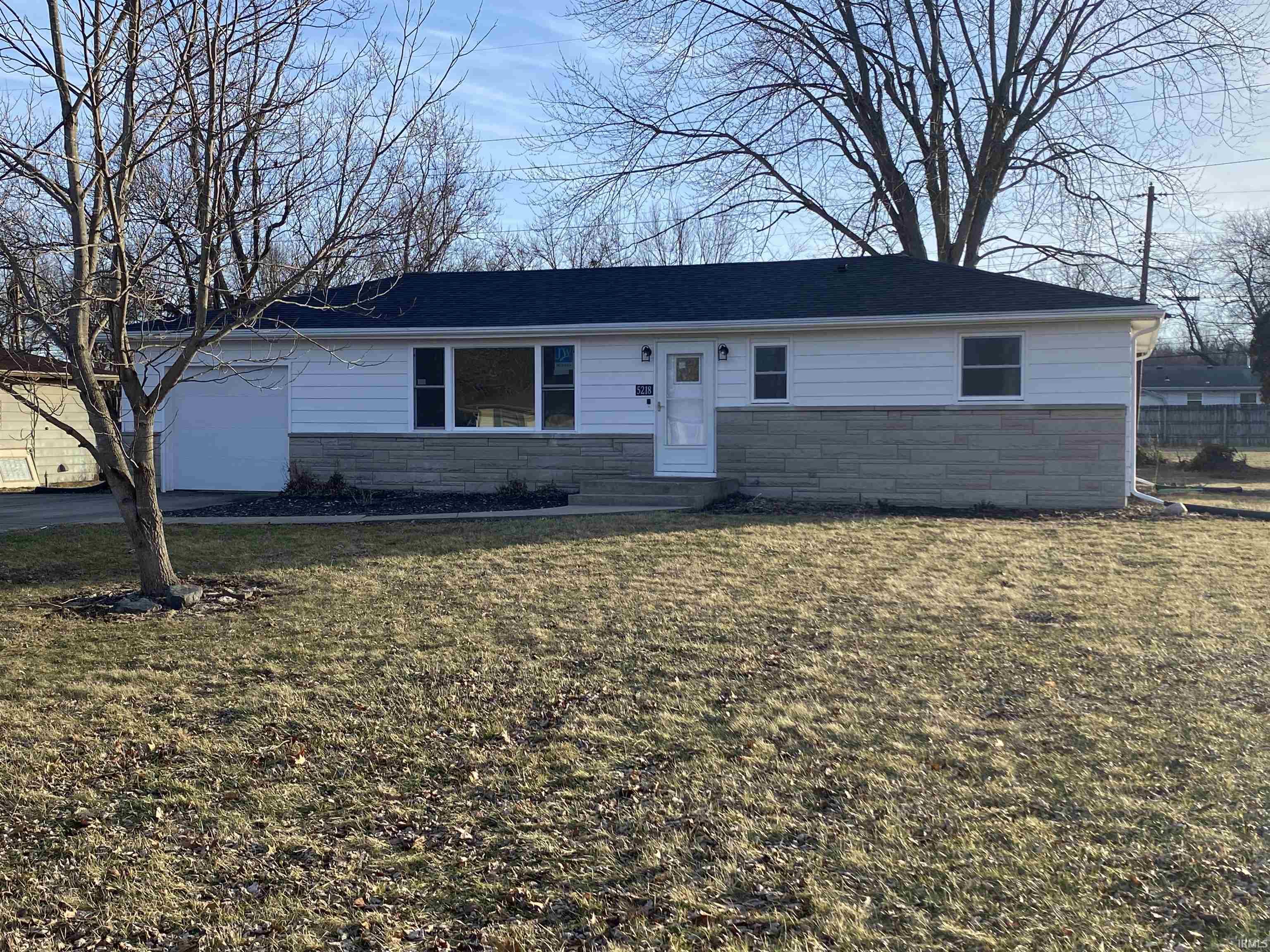 Ranch-style home with stone siding, a front lawn, and a garage