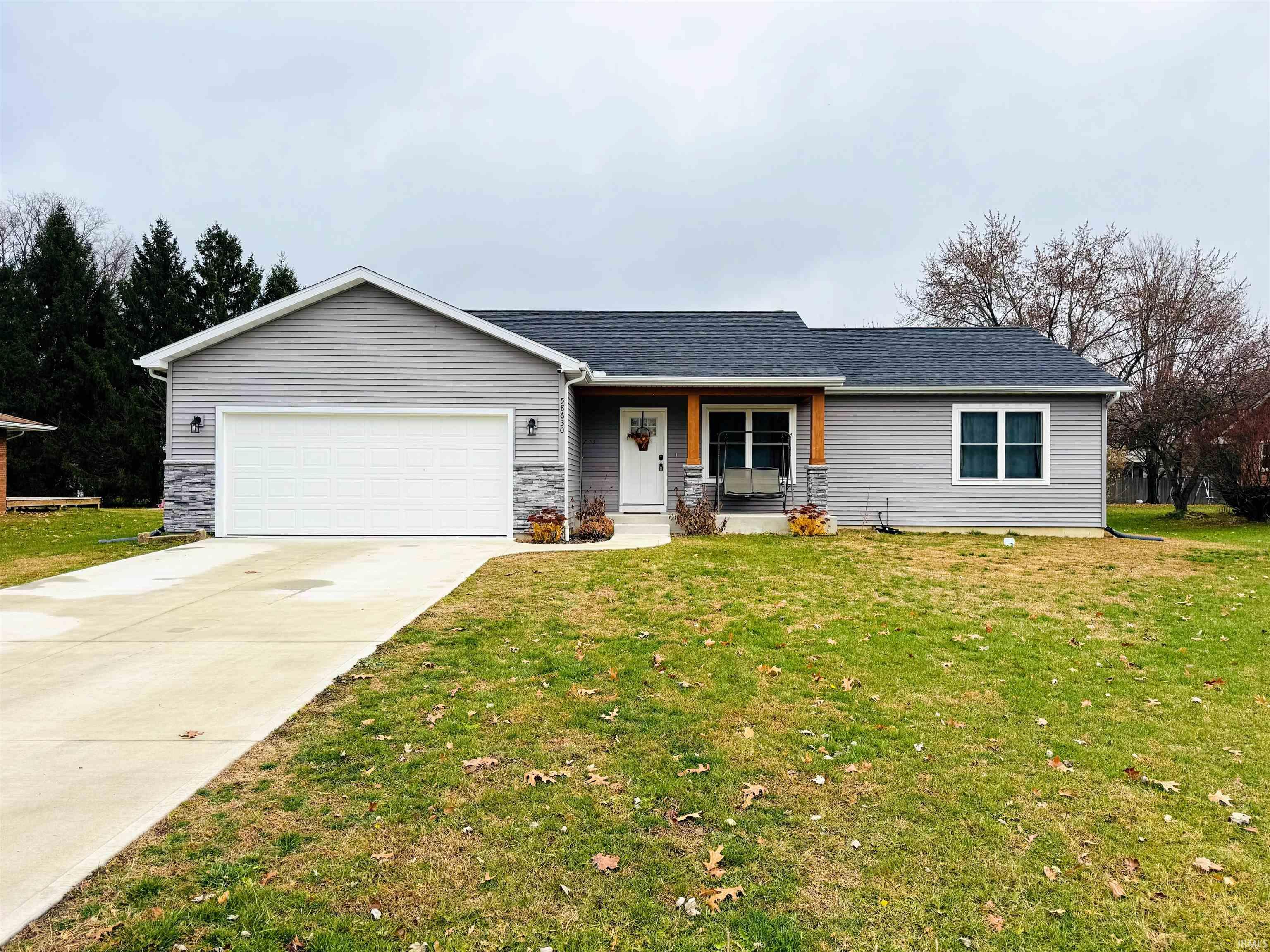 Single story home featuring a porch, driveway, stone siding, and a front lawn