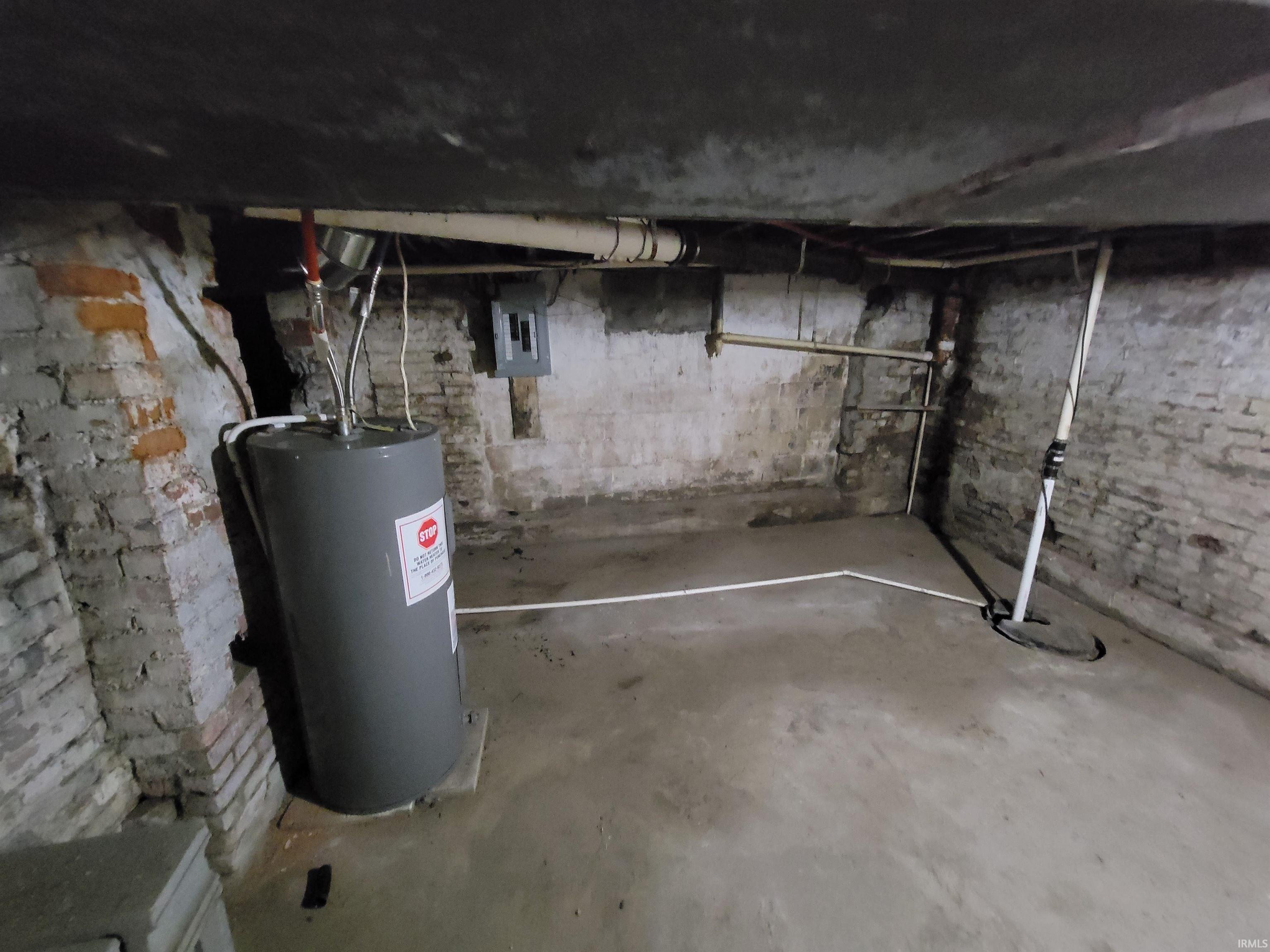Unfinished below grade area featuring water heater, electric panel, and drainage system