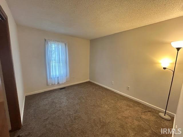 Spare room featuring dark colored carpet and a textured ceiling