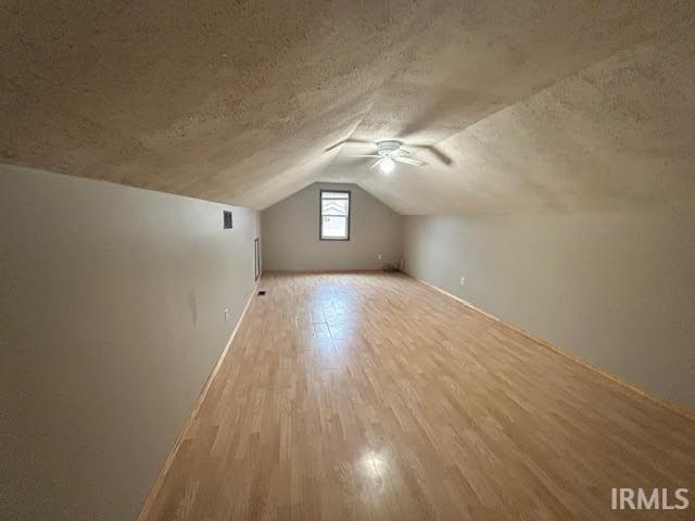 Bonus room with wood finished floors, a ceiling fan, and a textured ceiling
