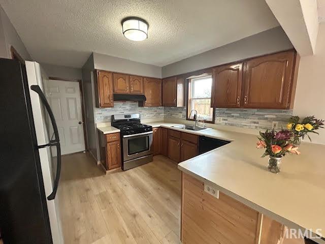 Kitchen with freestanding refrigerator, stainless steel gas stove, decorative backsplash, light countertops, and a textured ceiling
