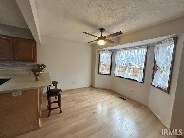 Unfurnished dining area with light wood-type flooring, ceiling fan, and a textured ceiling