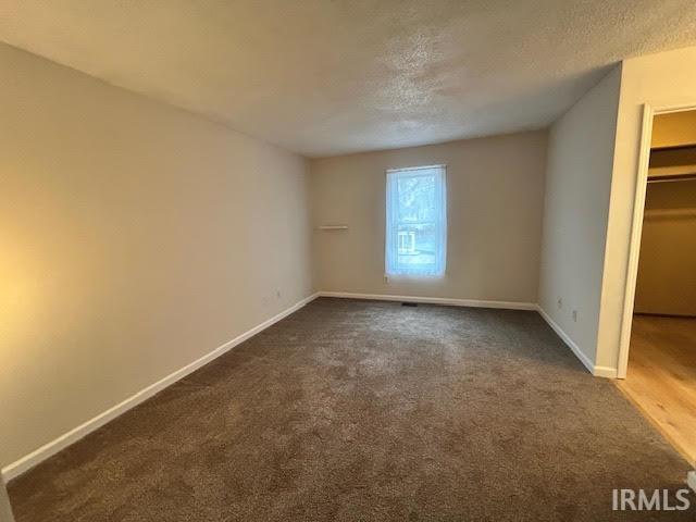 Unfurnished bedroom featuring a spacious closet, dark carpet, and a textured ceiling