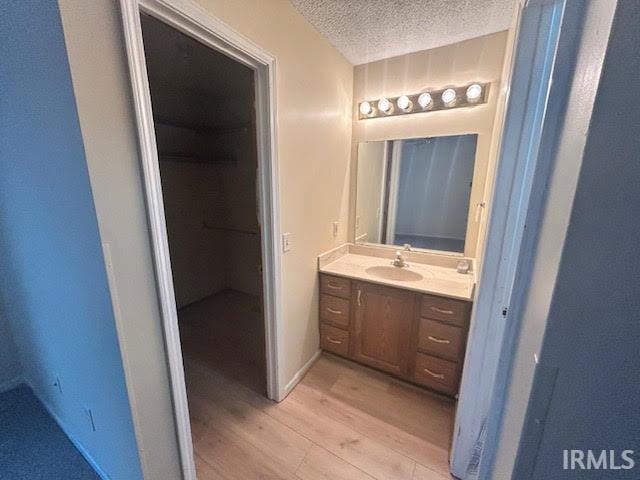 Full bathroom with a textured ceiling, light wood-type flooring, vanity, and a walk in closet