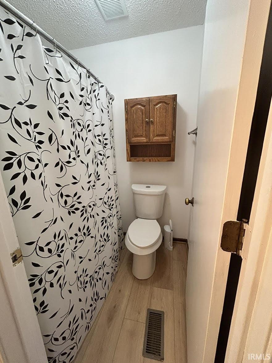 Bathroom featuring light wood-type flooring, a textured ceiling, and a shower with shower curtain
