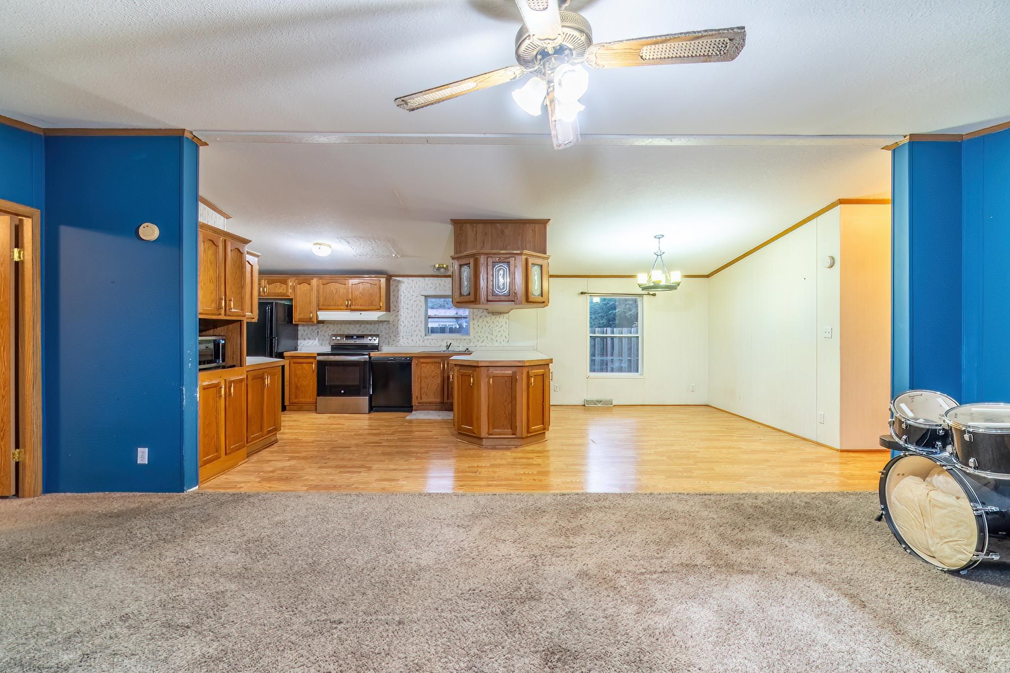Kitchen with brown cabinets, light colored carpet, black appliances, light countertops, and a ceiling fan