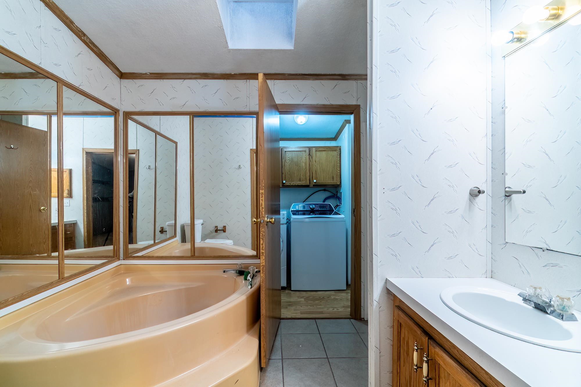 Full bathroom featuring wallpapered walls, washer / dryer, light tile patterned flooring, a garden tub, and vanity
