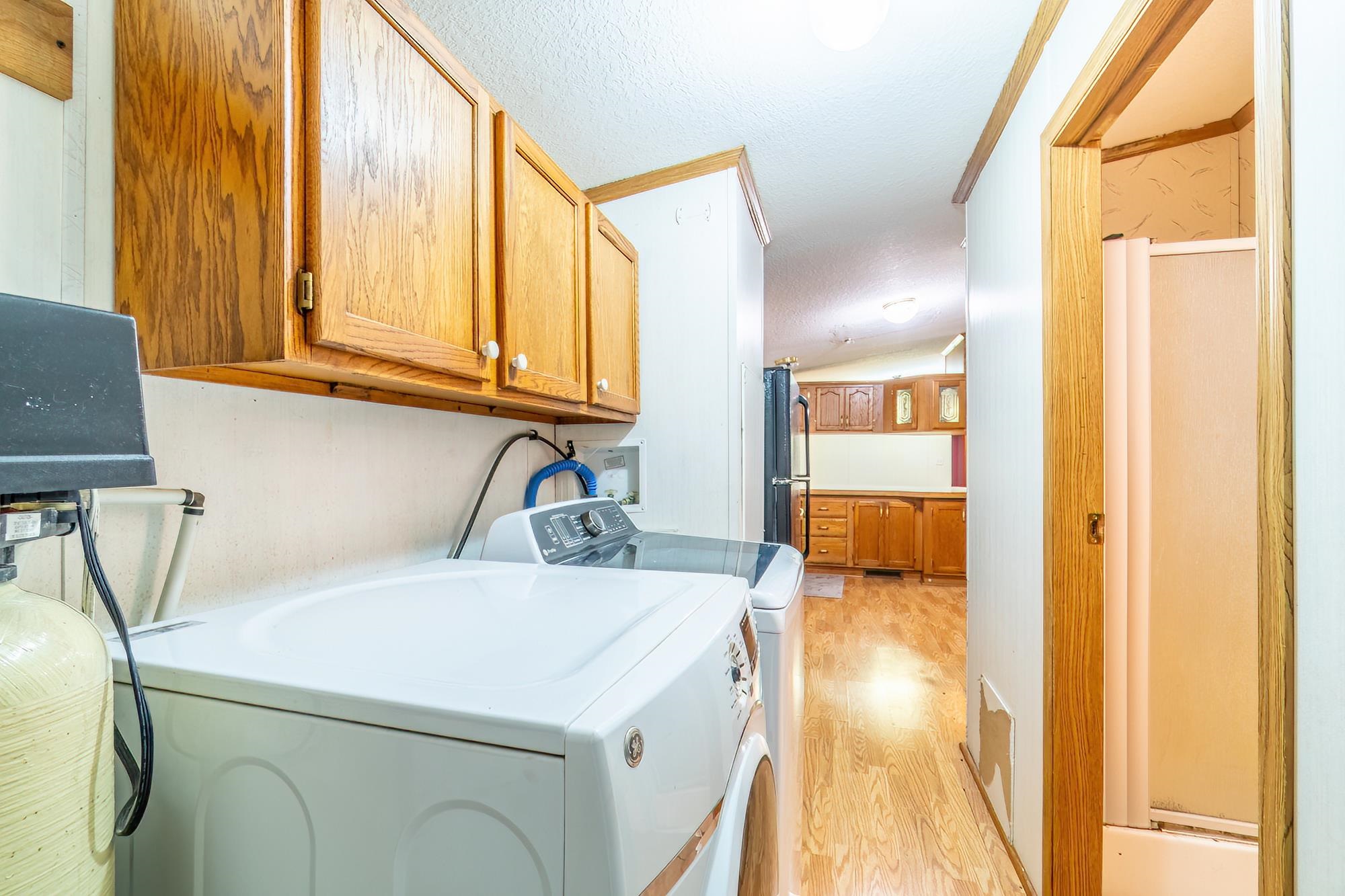 Laundry area featuring light wood-style floors, a textured ceiling, separate washer and dryer, cabinet space, and vaulted ceiling