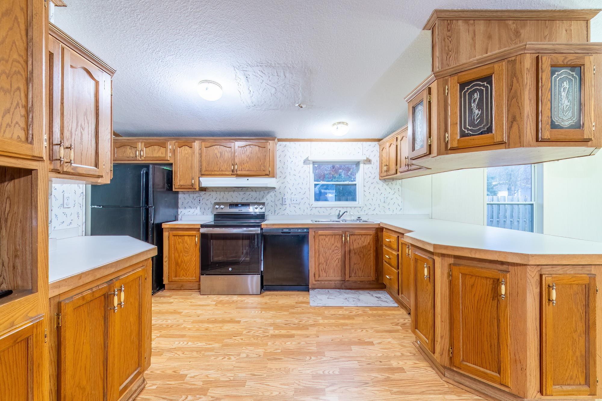 Kitchen featuring brown cabinetry, black appliances, light countertops, light wood-style flooring, and a textured ceiling