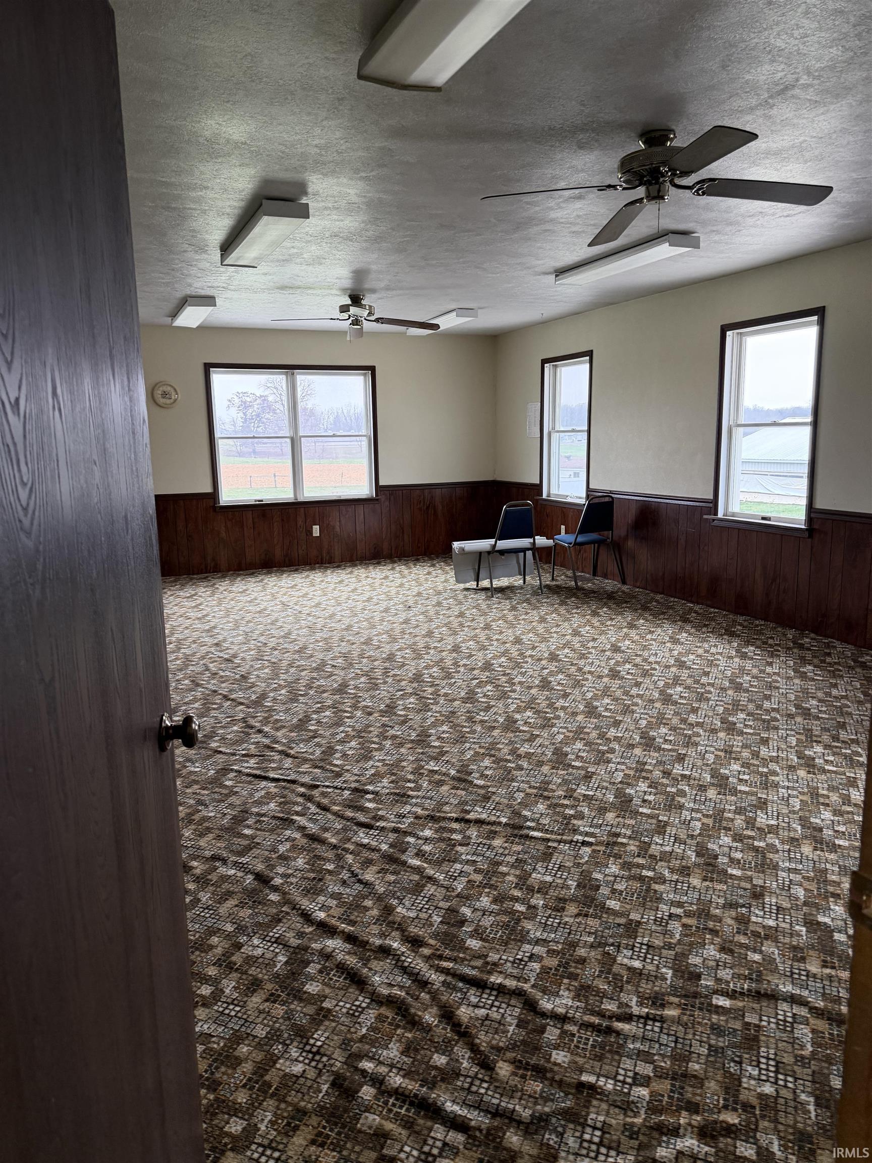 Spare room featuring wooden walls, a wainscoted wall, plenty of natural light, a textured ceiling, and ceiling fan