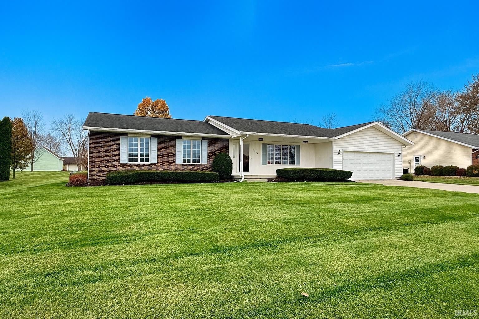 Ranch-style home featuring a front yard, a porch, brick siding, a garage, and driveway