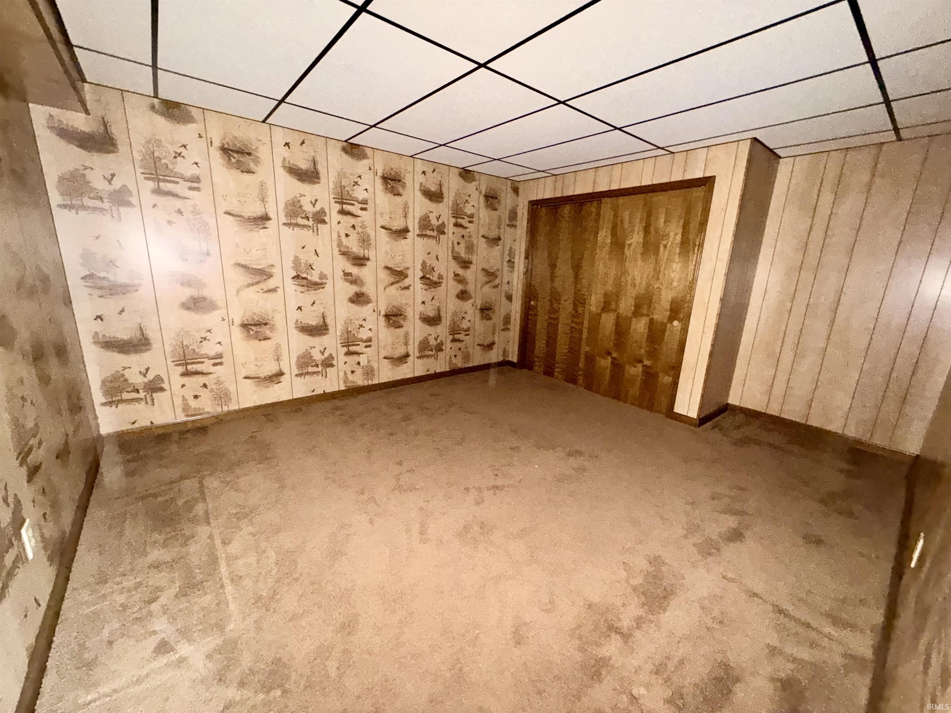 Spare room featuring a drop ceiling, carpet flooring, and wooden walls
