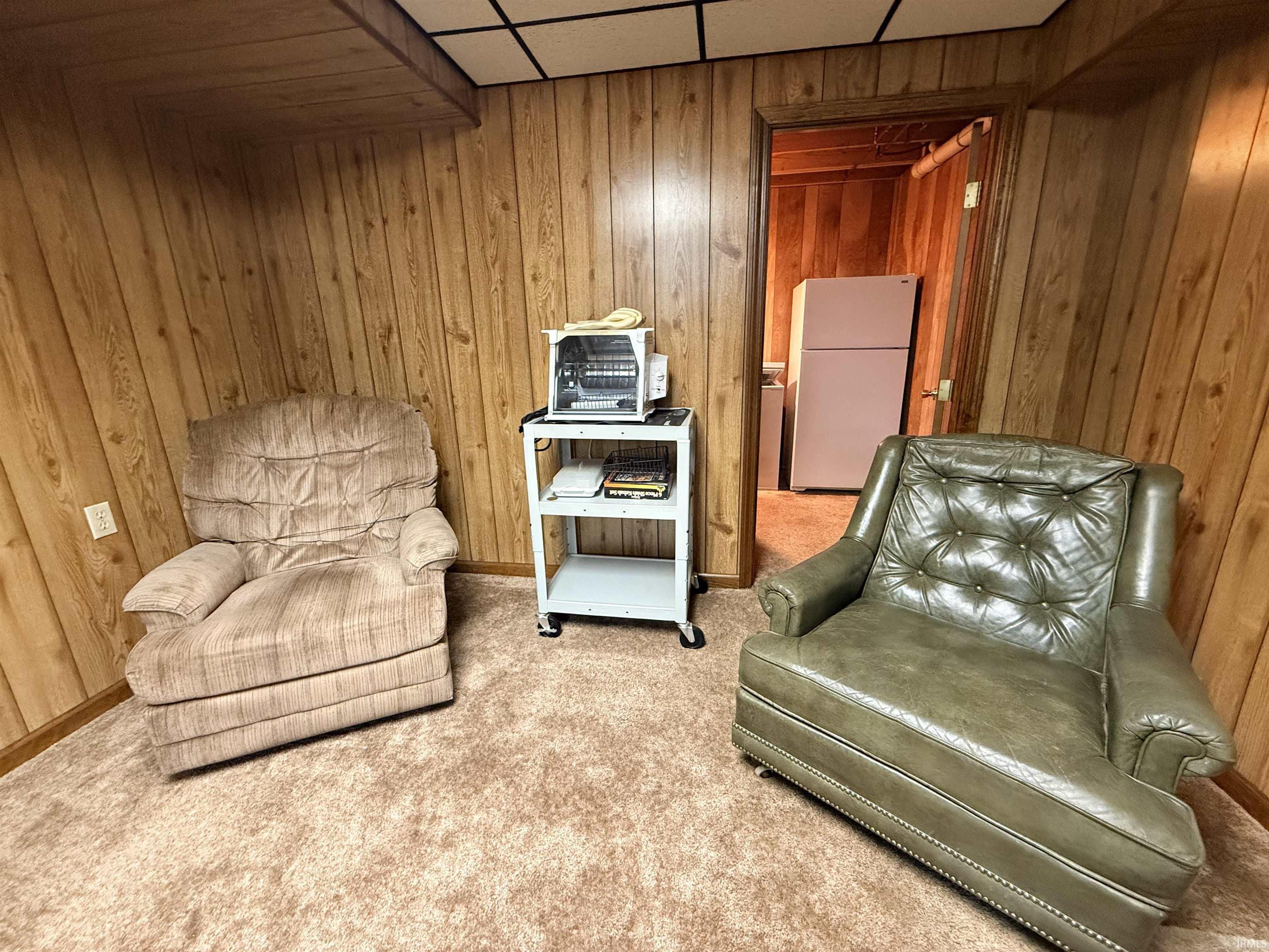 Sitting room featuring wooden walls, carpet flooring, and a drop ceiling