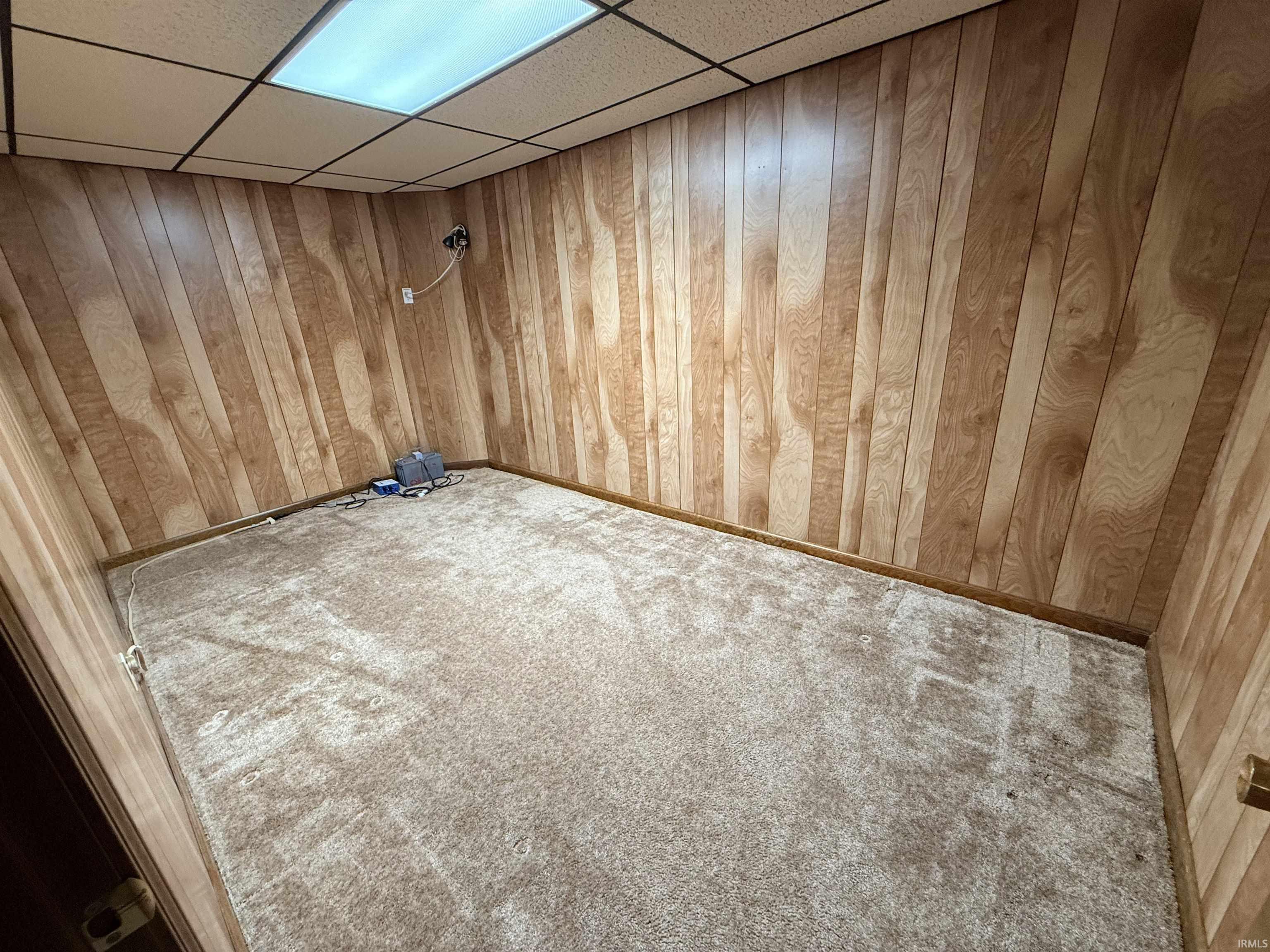 Spare room with a paneled ceiling, wood walls, and carpet floors