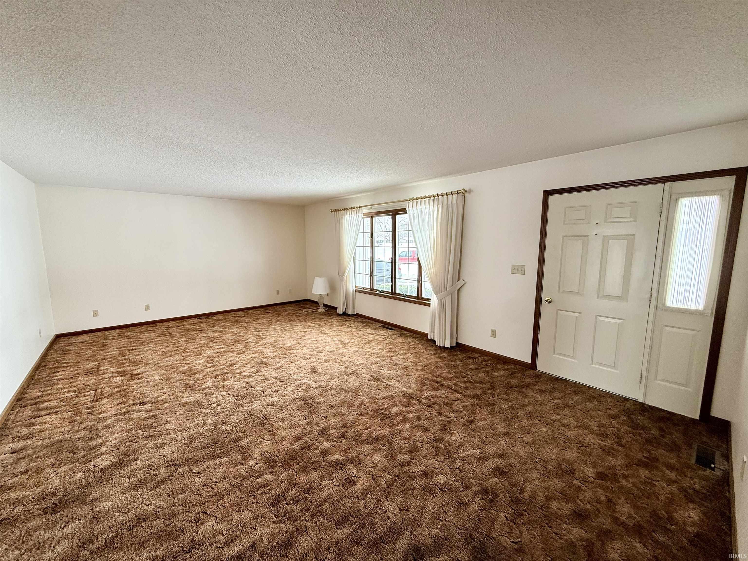 Foyer entrance with a textured ceiling and dark colored carpet